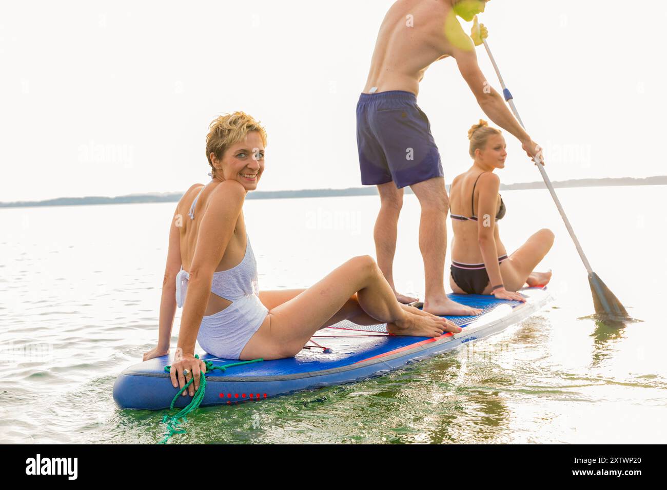 Tre amici si divertono a fare paddleboard insieme su un lago calmo. Foto Stock