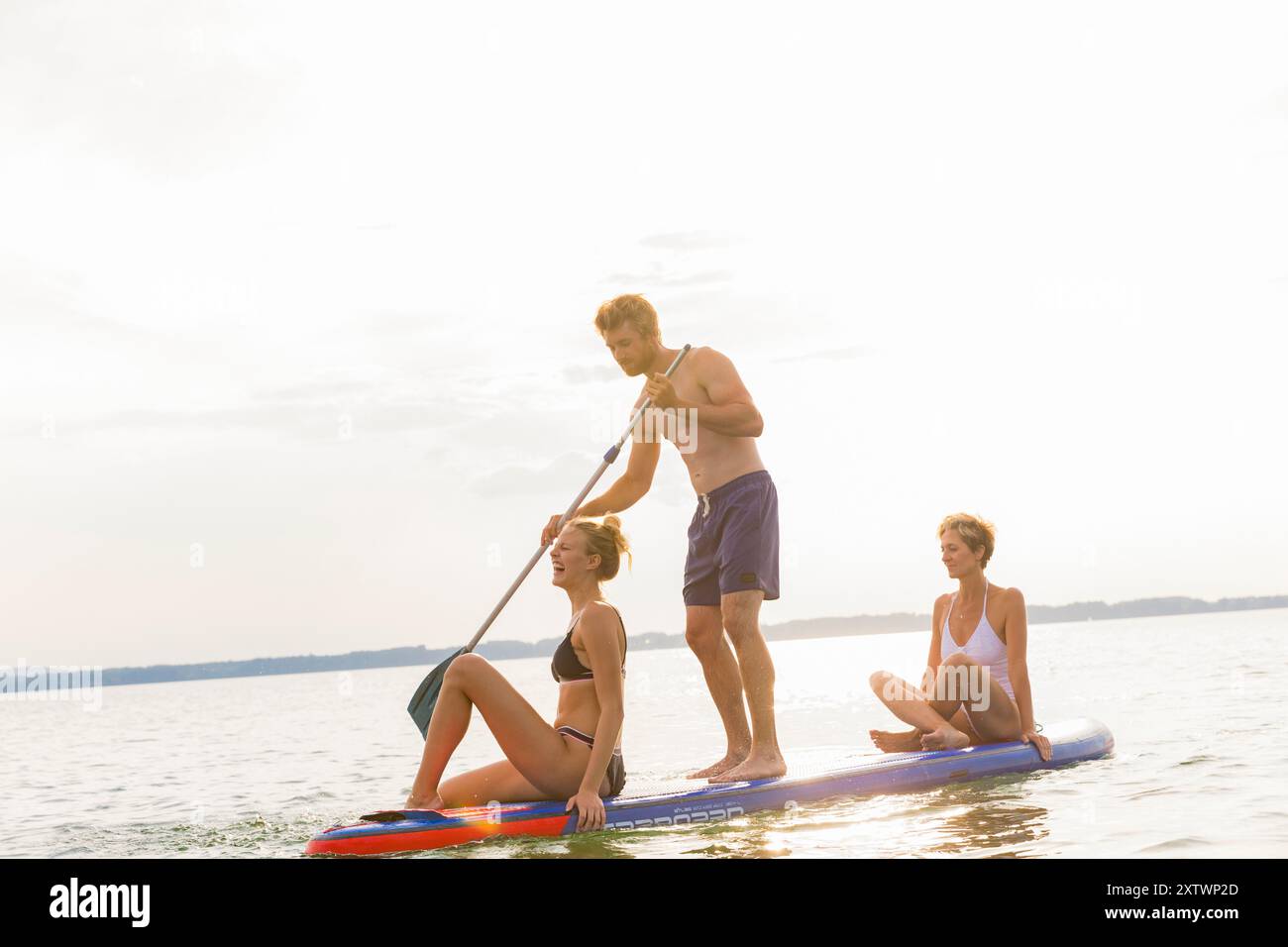 Trio ama andare in paddleboard insieme su un lago tranquillo al tramonto. Foto Stock