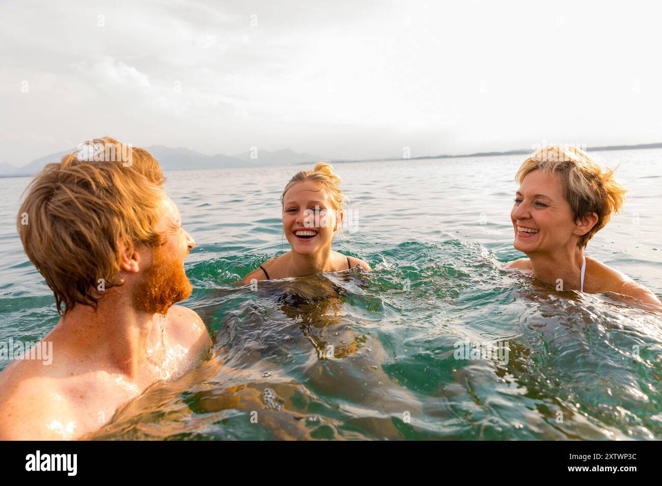 Tre persone si divertono a nuotare in mare, ridendo insieme durante una giornata di sole. Foto Stock