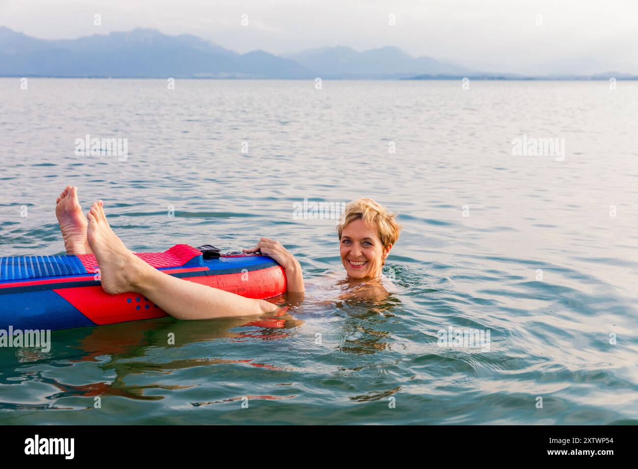 Donna che galleggia su un tappeto gonfiabile in un lago calmo con montagne sullo sfondo. Foto Stock