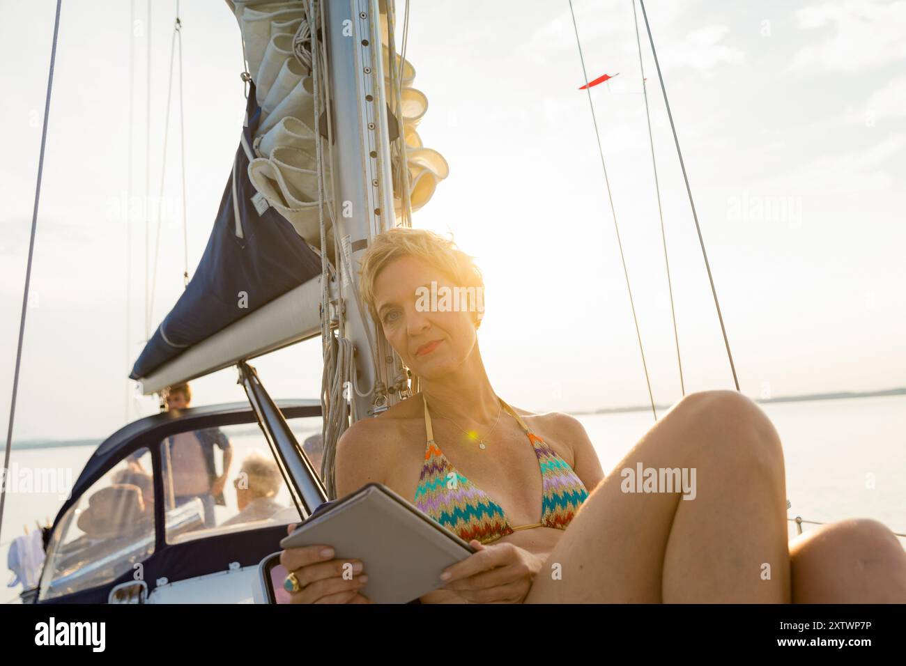 Donna che si rilassa con un lettore elettronico su una barca a vela al tramonto. Foto Stock