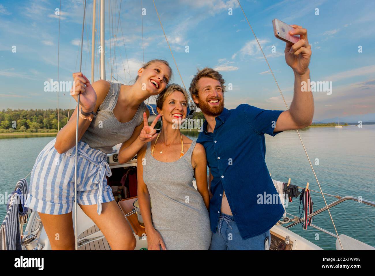 Tre amici che scattano un selfie su una barca a vela con un cielo blu chiaro sullo sfondo. Foto Stock