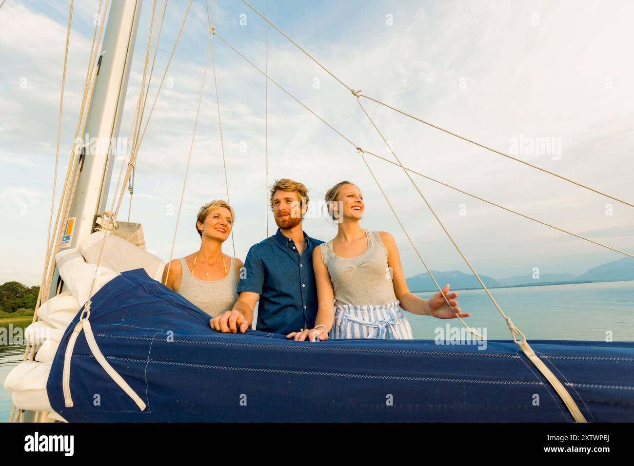 Tre amici si godono una giornata di sole su una barca a vela con un cielo azzurro e un mare tranquillo sullo sfondo. Foto Stock