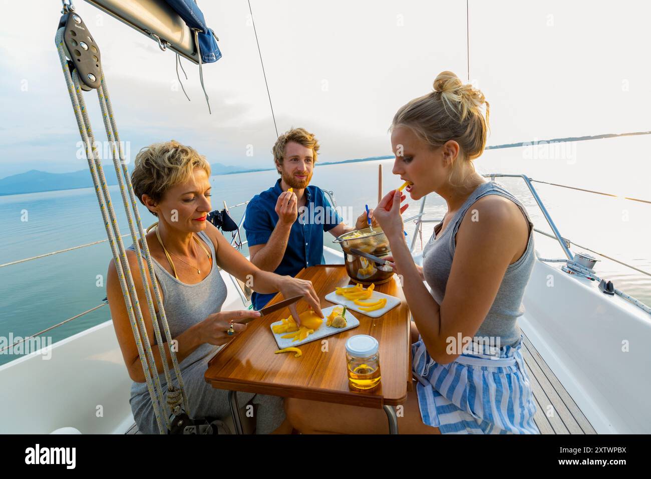 Gruppo di amici che gusteranno un pasto su una barca a vela al tramonto con mare calmo sullo sfondo Foto Stock