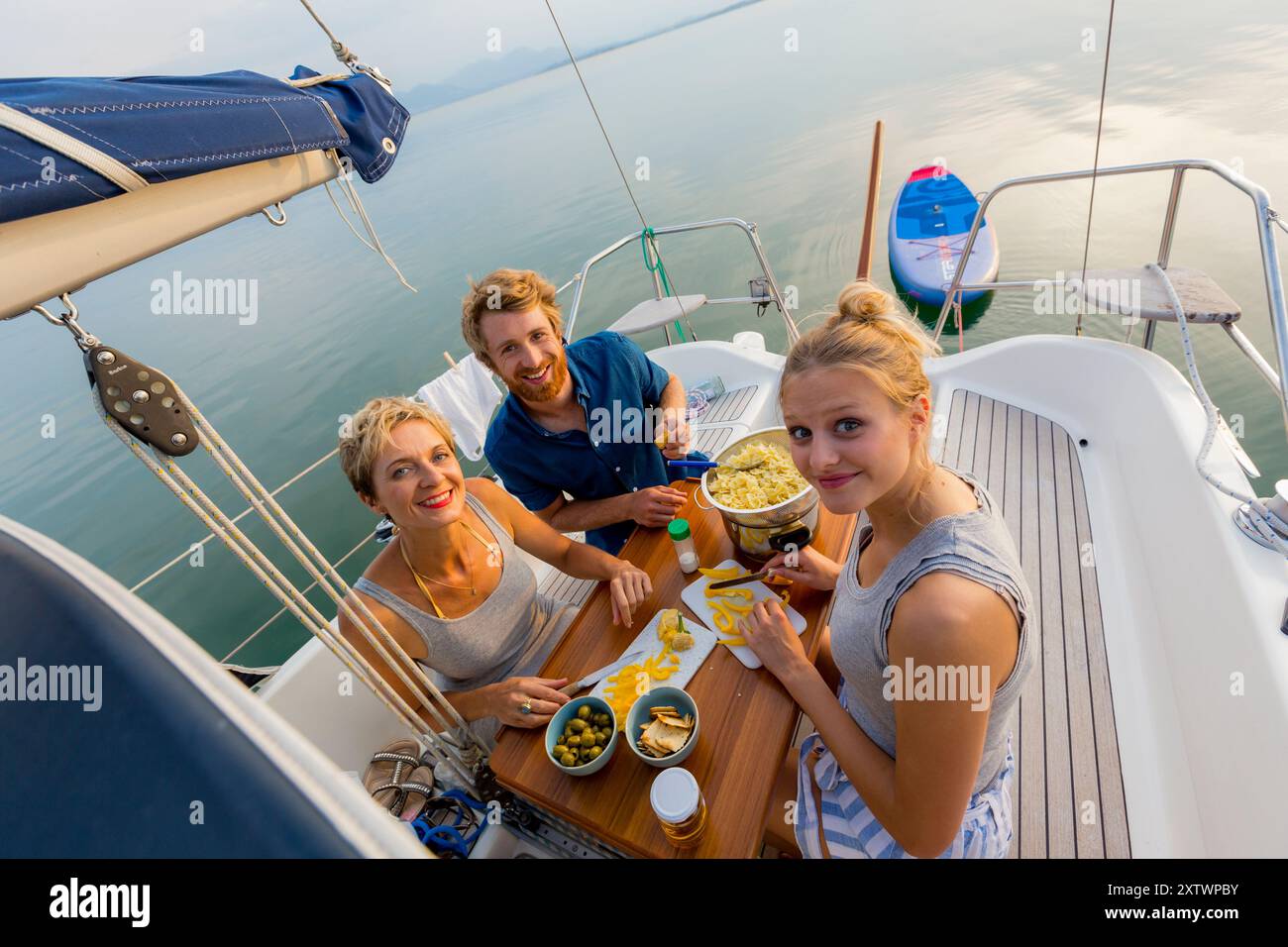 Gruppo di amici che gusta spuntini e bevande sul ponte di uno yacht in mare durante una giornata di sole. Foto Stock