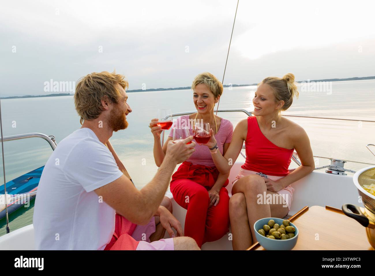 Tre amici si godono un drink e chiacchierano su una barca al tramonto. Foto Stock