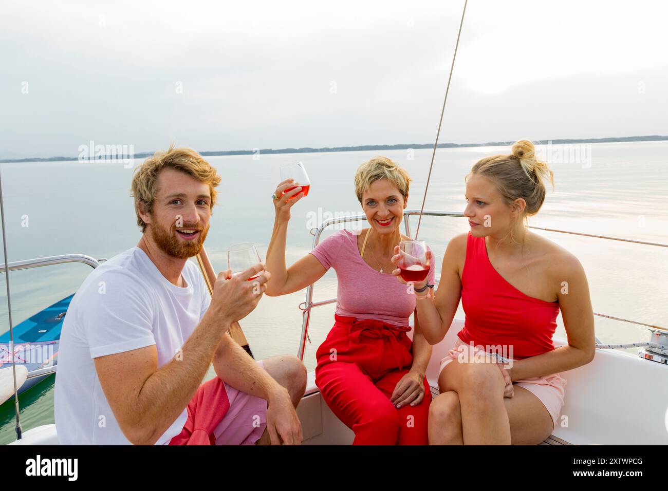 Tre amici si godranno un drink e si divertiranno su una barca con un lago panoramico sullo sfondo durante il tramonto. Foto Stock