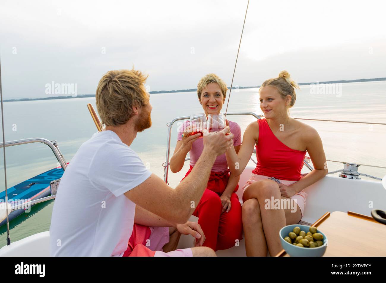 Tre amici che si godono un brindisi con bevande su una barca a vela al tramonto Foto Stock