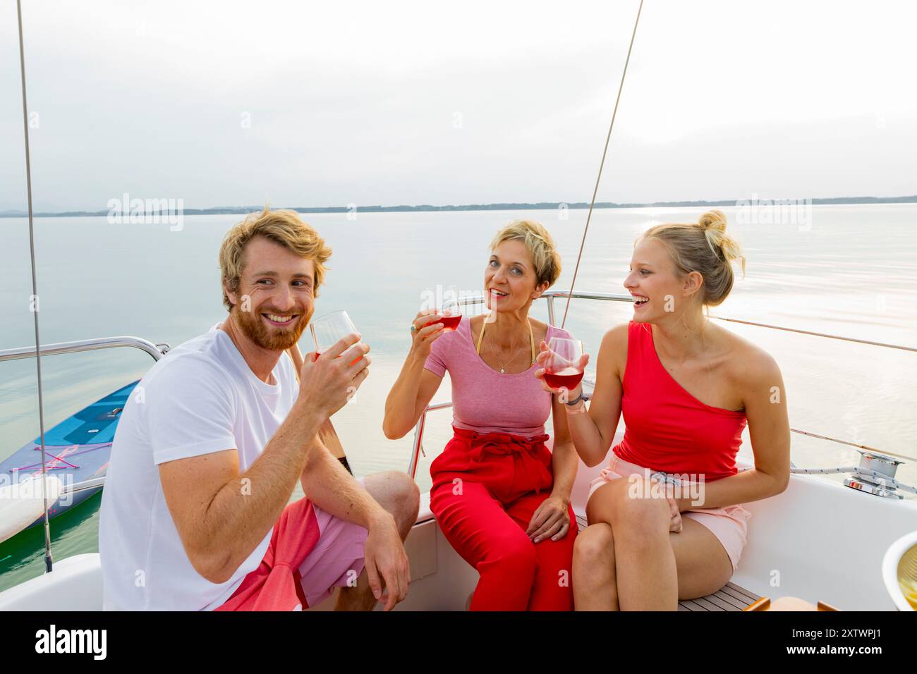 Tre amici si godono un drink su uno yacht con un lago tranquillo sullo sfondo al tramonto. Foto Stock