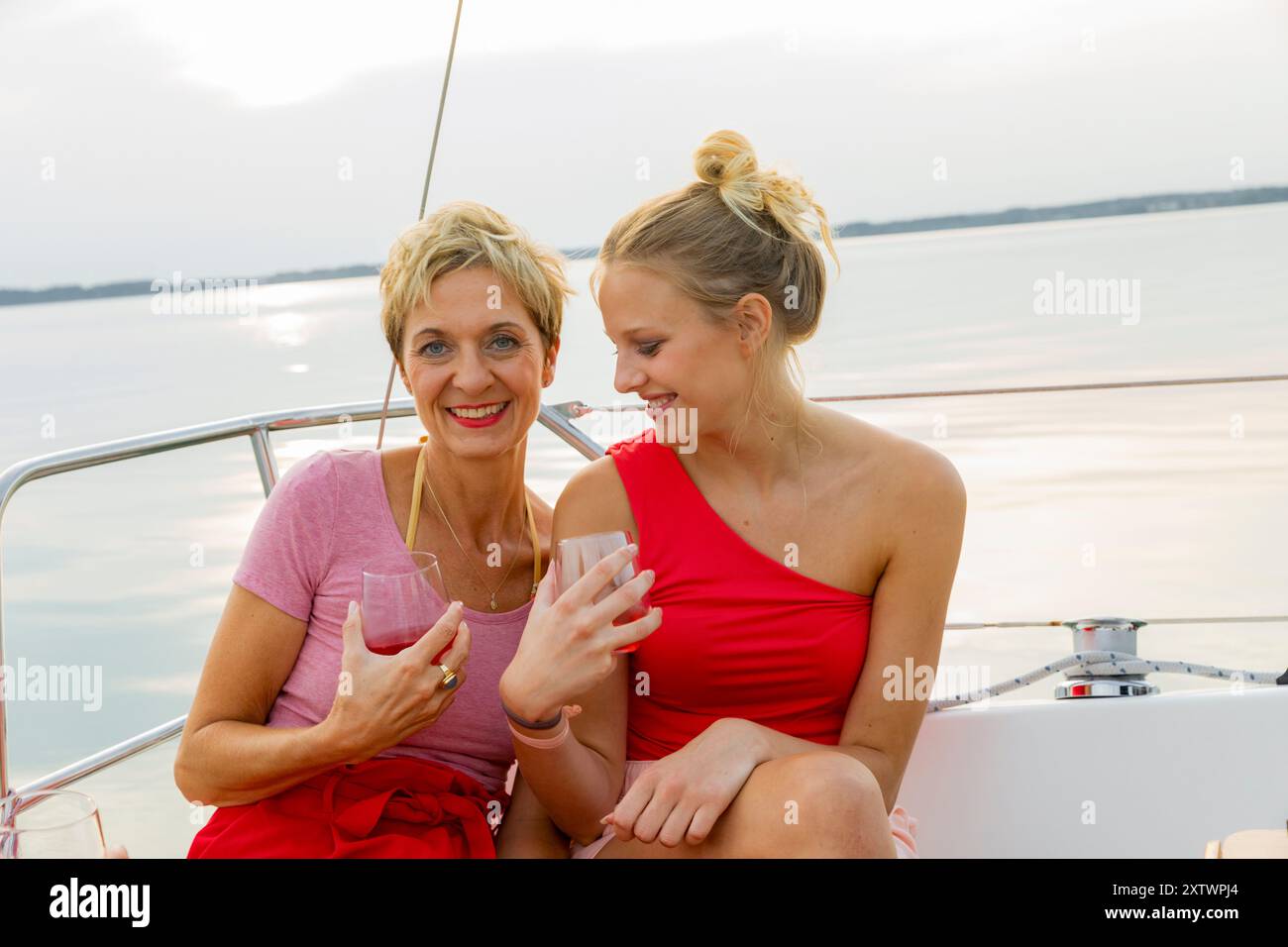 Due donne sorridono e tengono in mano gli occhiali su una barca con vista sul lago al tramonto. Foto Stock