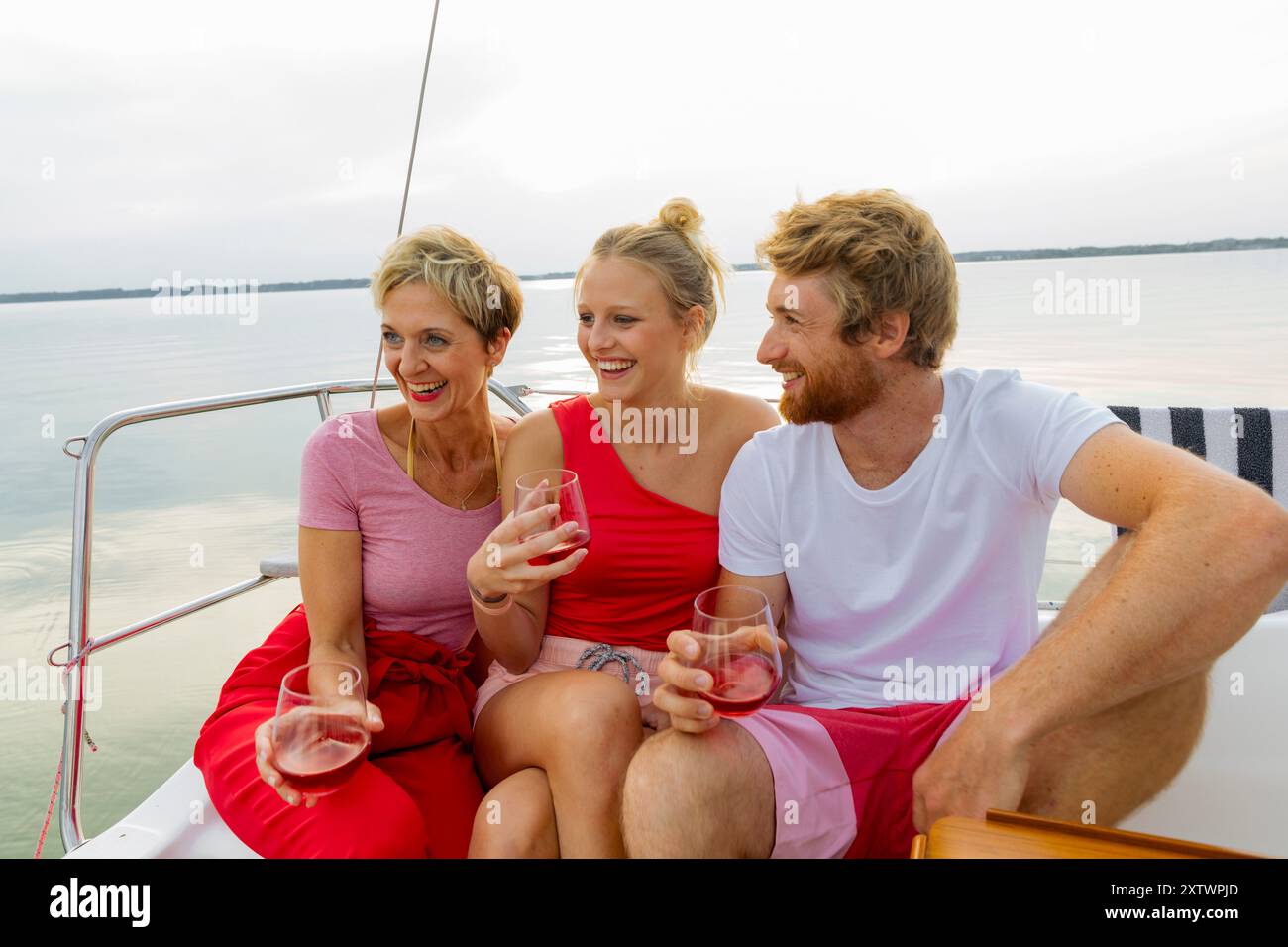 Tre amici che si godono bevande e risate su una barca con un tranquillo sfondo d'acqua. Foto Stock