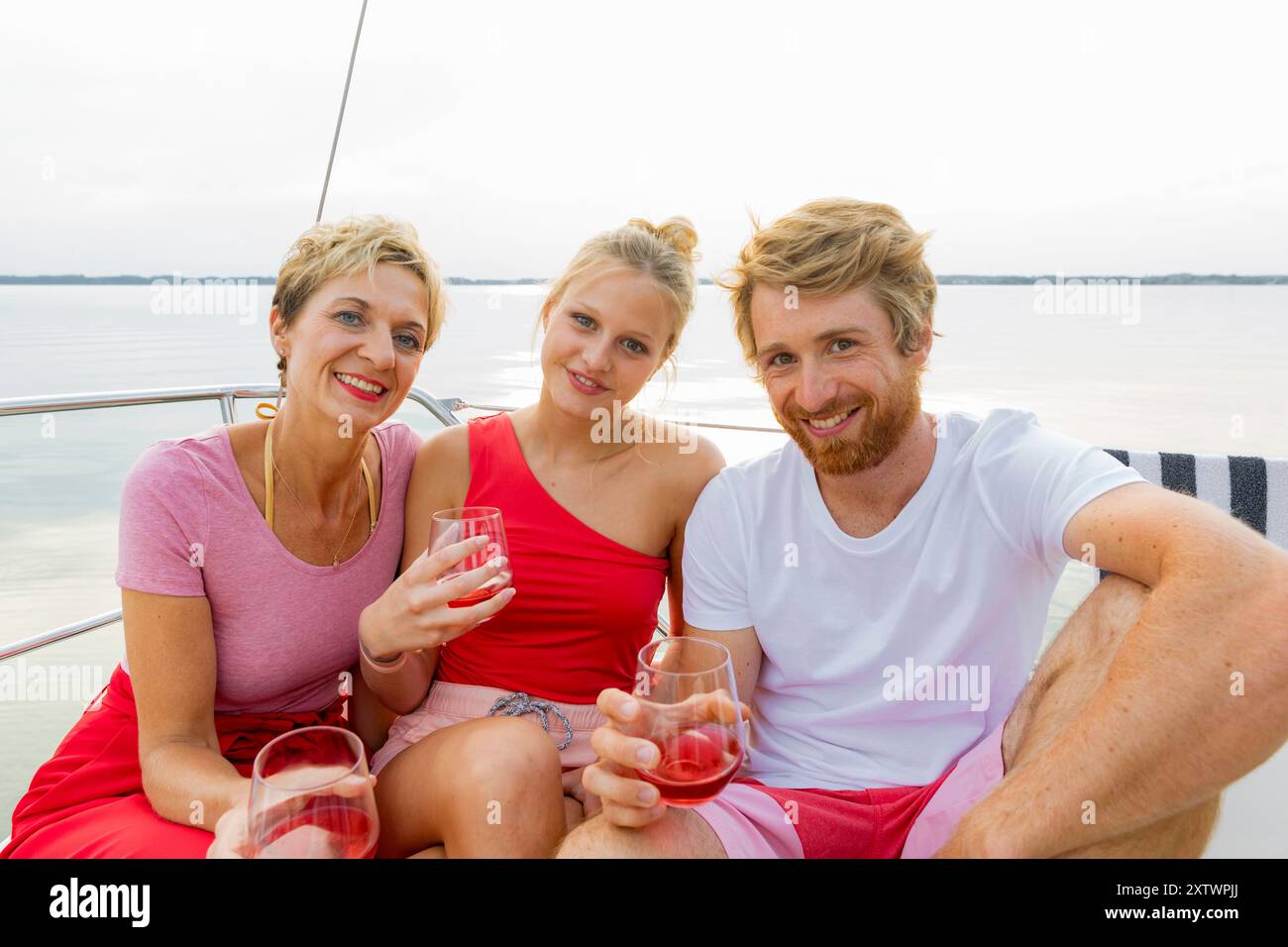 Tre amici si godono un drink su una barca con un lago sullo sfondo. Foto Stock