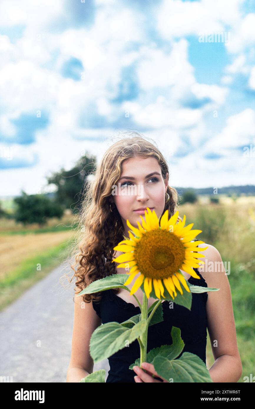 Ritratto di una giovane donna che tiene in mano un girasole giallo fresco e si gode il momento. Foto Stock