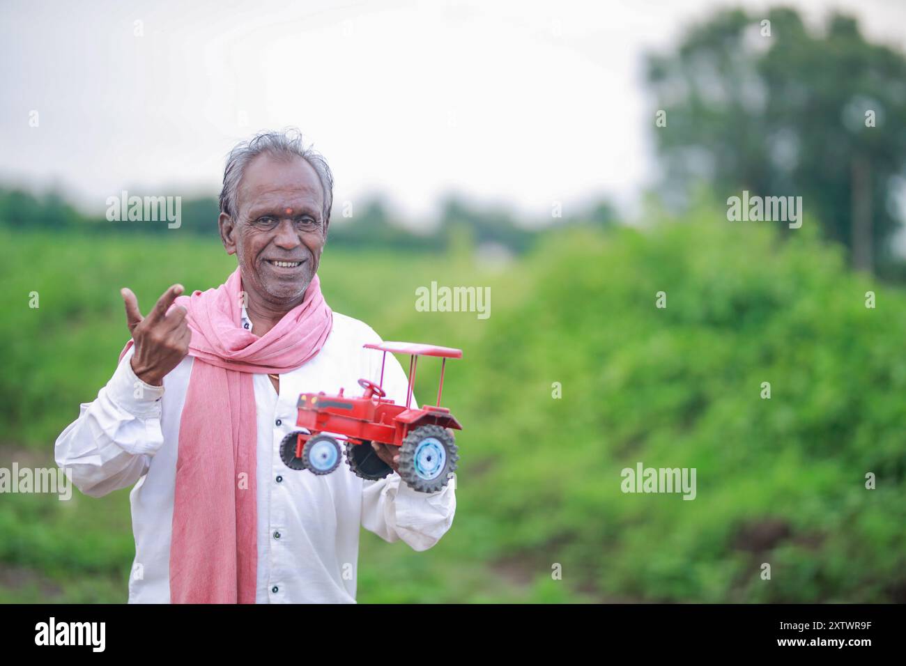 Agricoltore indiano che detiene un mini trattore giocattolo per prestito e banche , successo di poveri e vecchi agricoltori Foto Stock