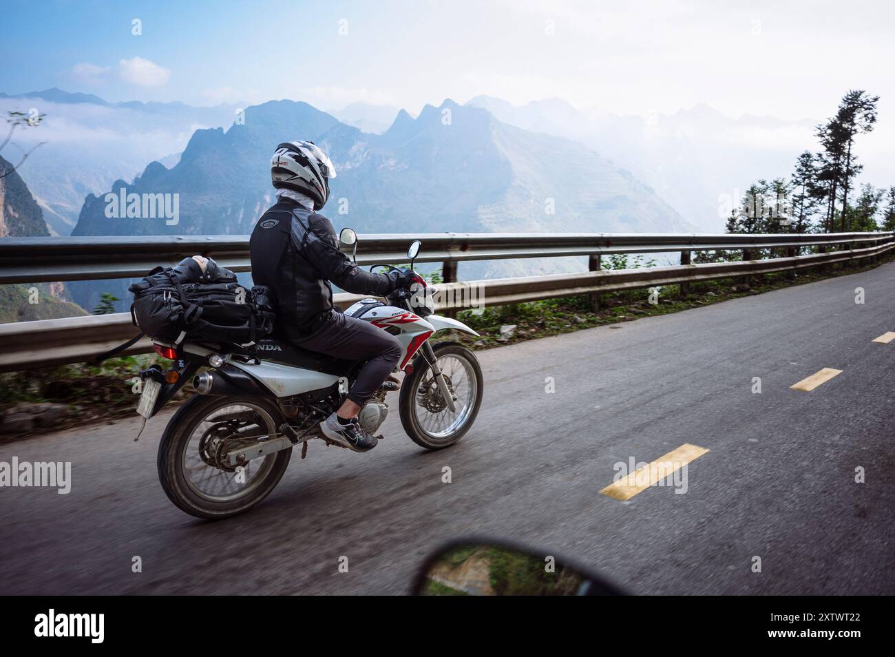 Motociclista su una strada panoramica di montagna con paesaggio pittoresco sullo sfondo. Foto Stock