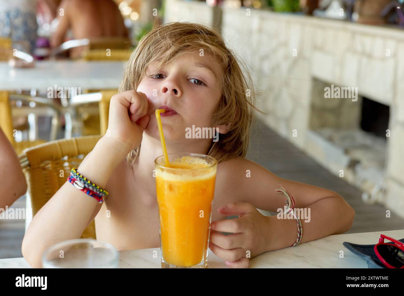 Ragazzo che sorseggia un succo d'arancia fresco attraverso una cannuccia in un Cafè. Foto Stock