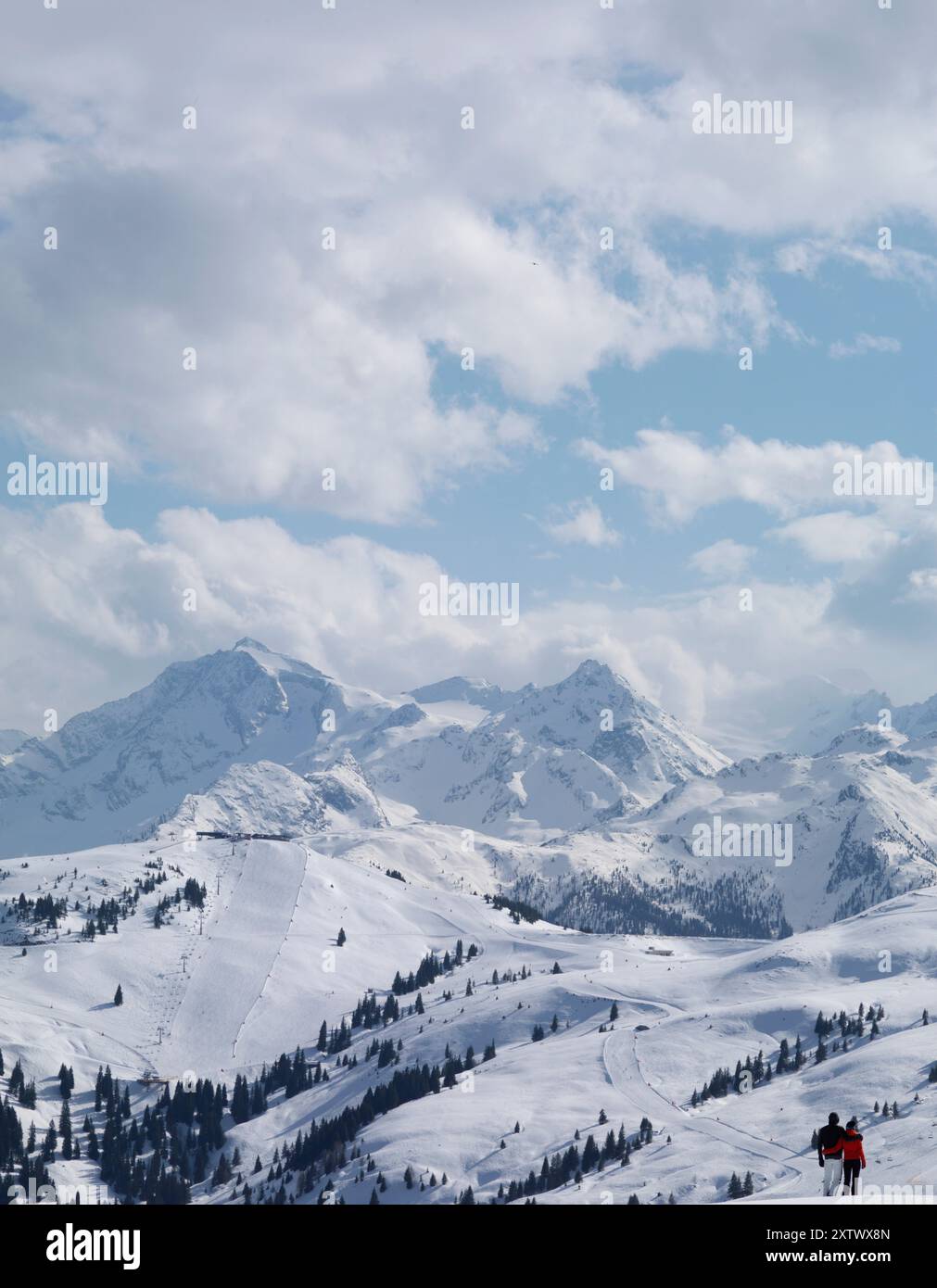 Sciatori su una pista innevata con montagne maestose sotto un cielo blu nuvoloso. Foto Stock