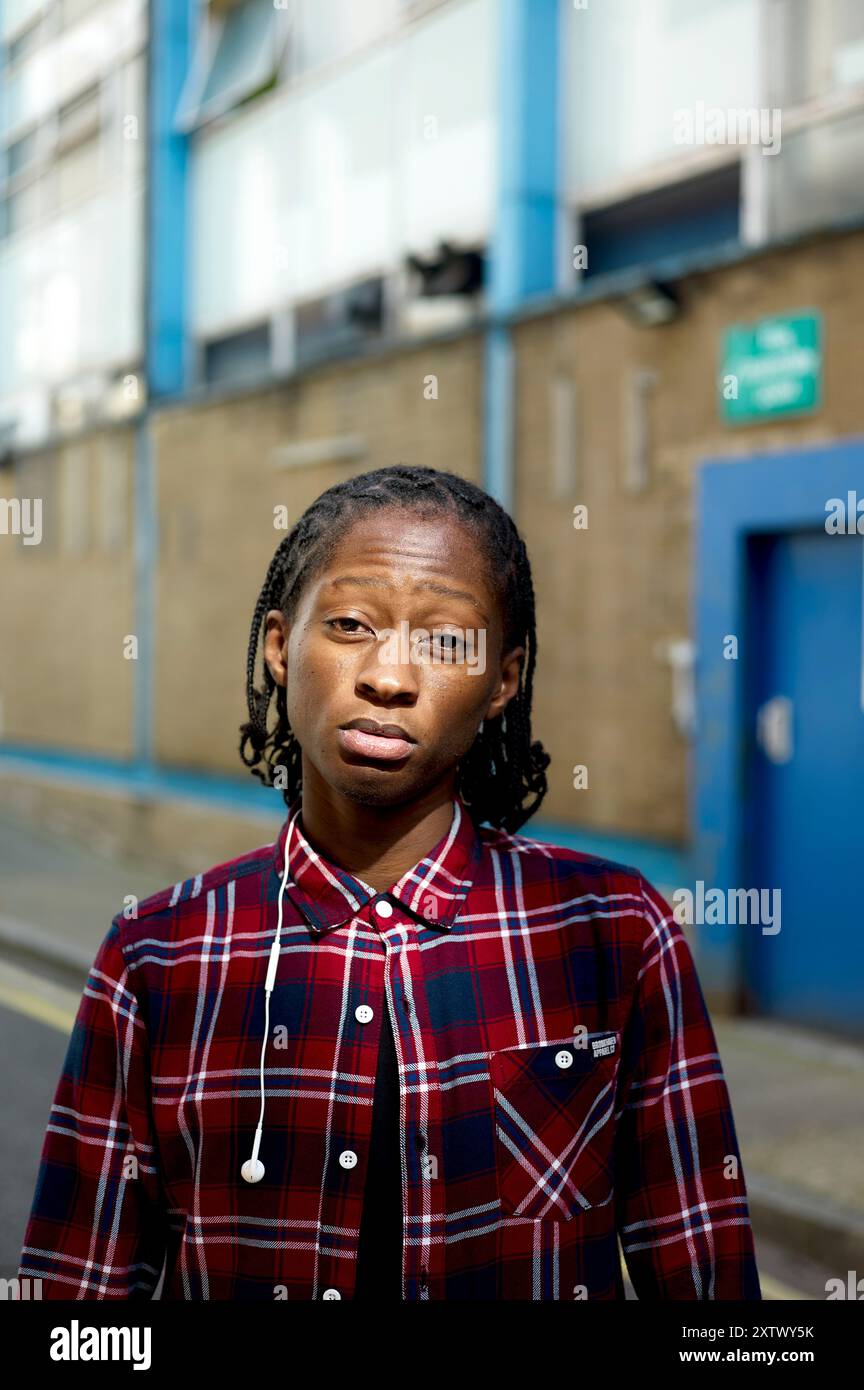 Persona con dreadlock che indossa una camicia a quadri rossa in piedi su una strada urbana con edifici sullo sfondo. Foto Stock