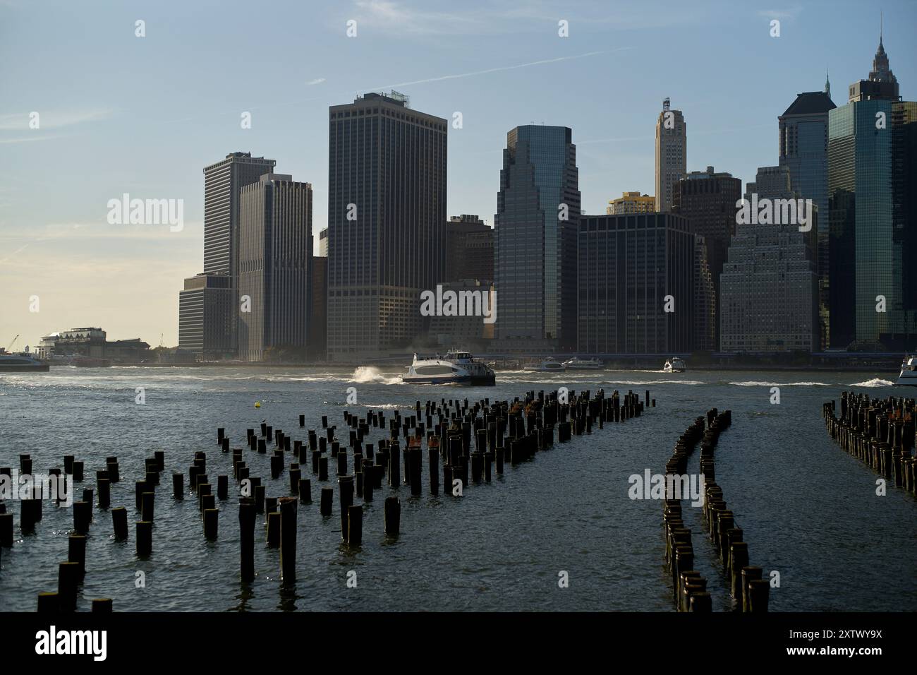 Vista al tramonto dello skyline di New York con i resti di un molo sagomato in primo piano e le barche sull'acqua. Foto Stock