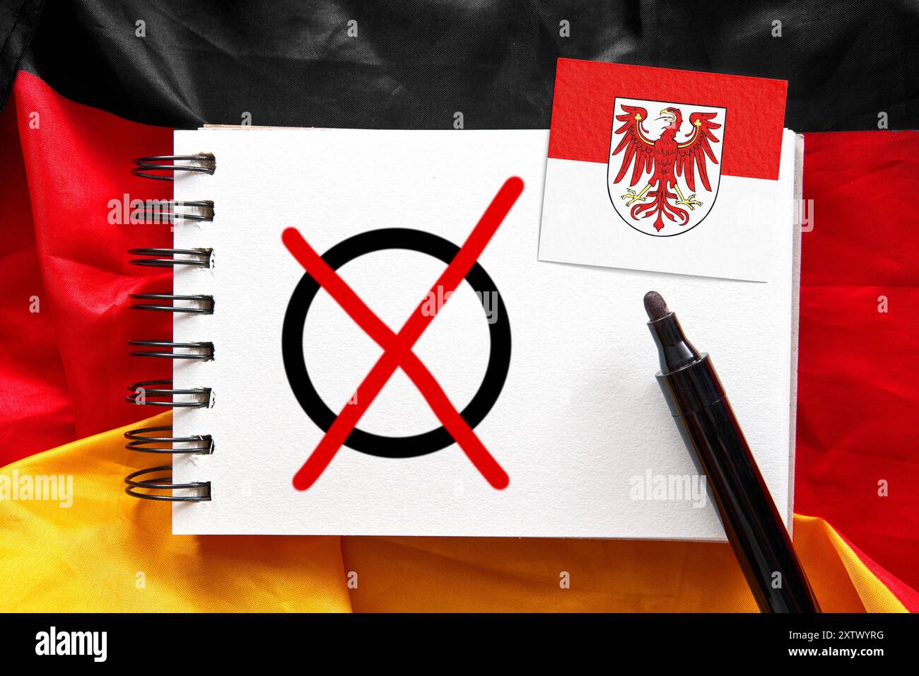 16 agosto 2024: Bandiera della Repubblica Federale di Germania con un blocco note su cui si può vedere una croce elettorale accanto a una penna con la bandiera dello Stato federale di Brandeburgo. Immagine simbolica delle elezioni statali. FOTOMONTAGGIO *** Flagge der Bundesrepublik Deutschland mit einem Notizblock auf dem ein Wahlkreuz neben einem Stift zu sehen ist mit der Flagge vom Bundesland Brandenburg. Symbolbild Landtagswahl. FOTOMONTAGE Foto Stock