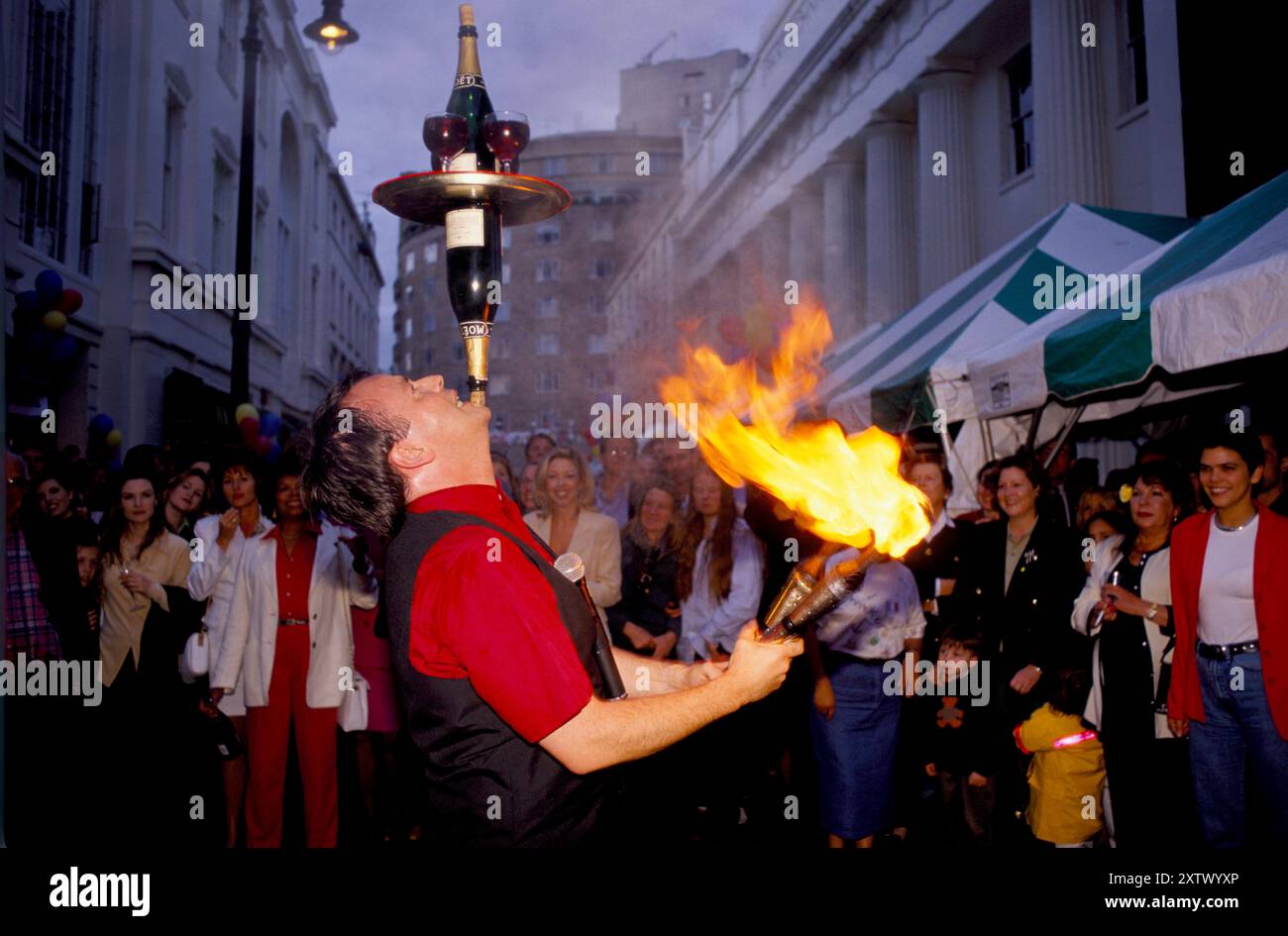 Street Party 1990s Regno Unito. Motcomb Street, festa annuale di strada a Belgravia, un giocoliere e mangiatore di fuoco bilancia due bottiglie e un vassoio con due bicchieri di vino rosso sul mento per intrattenere la folla. Belgravia, Londra, Inghilterra luglio 1998. HOMER SYKES Foto Stock