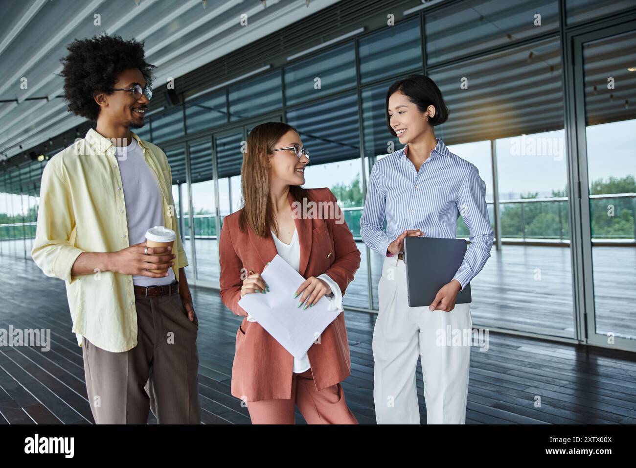 Un gruppo eterogeneo di colleghi chiacchiera sulla terrazza sul tetto, godendosi la vista e trascorrendo un momento informale fuori dall'ufficio. Foto Stock