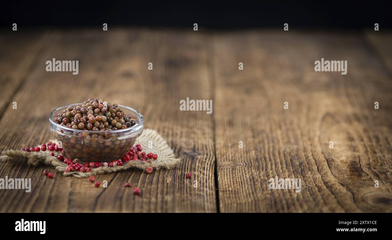 Grani di pepe rosa freschi (conservati) su un vecchio e rustico tavolo in legno, messa a fuoco selettiva, foto ravvicinata Foto Stock