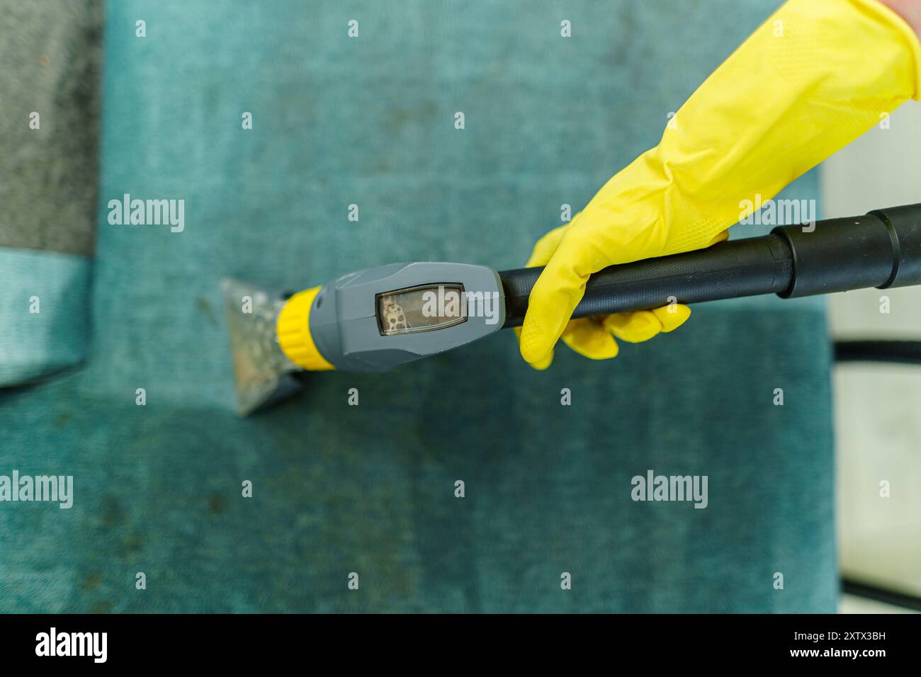 Primo piano di governante che tiene moderno aspirapolvere lavaggio e pulire il divano sporco con detergente professionale. Pulizia a molla professionale a casa Foto Stock