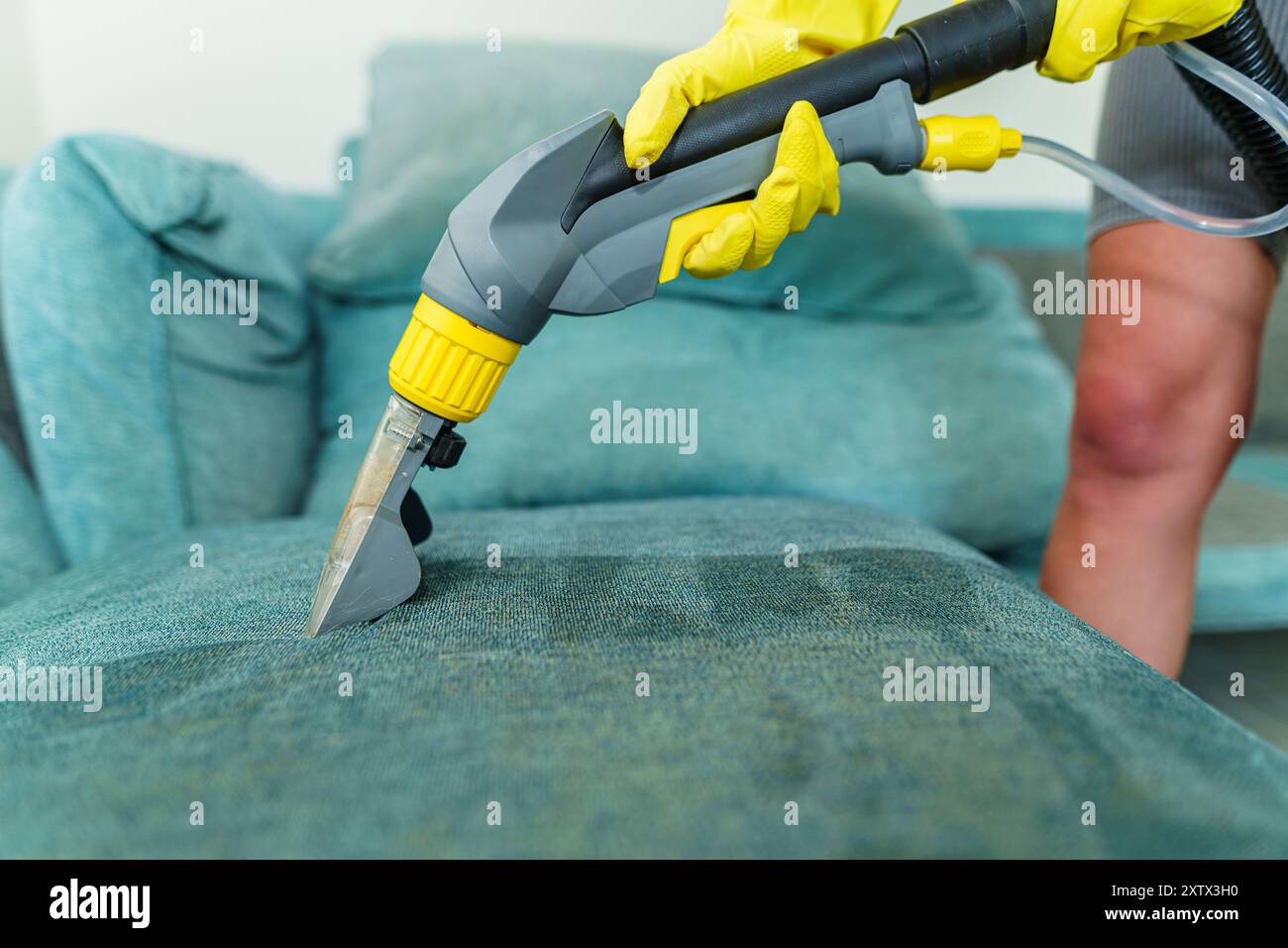 Primo piano di governante che tiene moderno aspirapolvere lavaggio e pulire il divano sporco con detergente professionale. Pulizia a molla professionale a casa Foto Stock