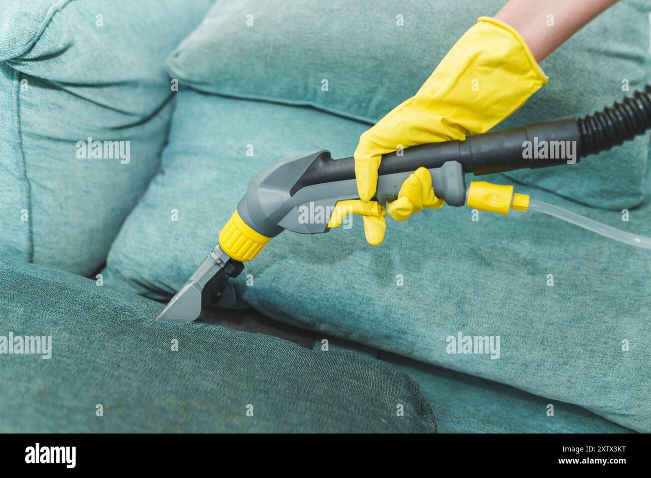 Primo piano di governante che tiene moderno aspirapolvere lavaggio e pulire il divano sporco con detergente professionale. Pulizia a molla professionale a casa Foto Stock