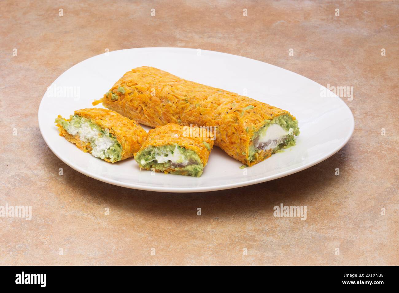 Primo piano di un appetitoso piatto di spuntini arrotolati con un vivace ripieno di guacamole e formaggio bianco, avvolto in uno strato esterno di carota color arancia Foto Stock