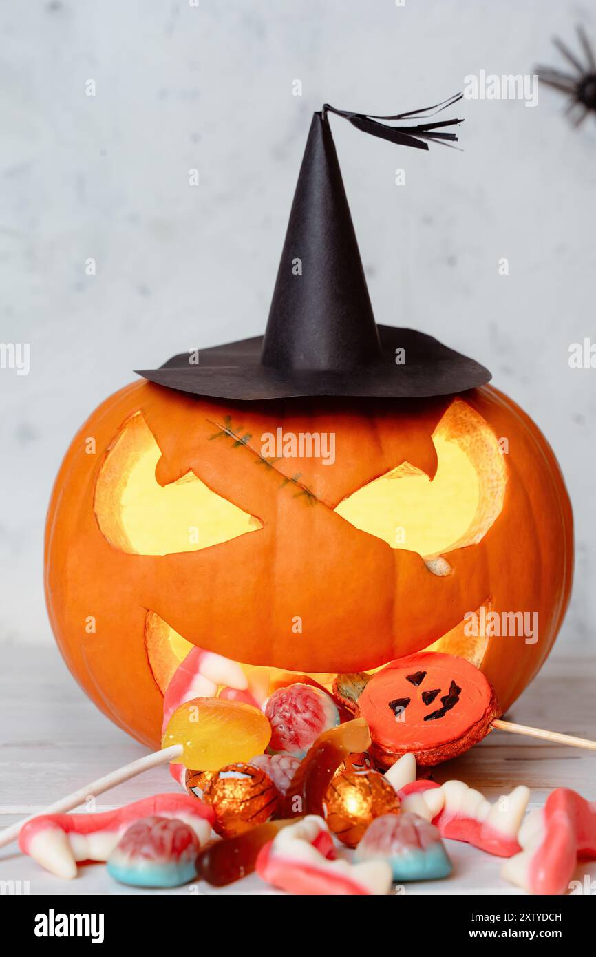 Zucca luccicante scolpita di Halloween dall'aspetto spettrale che sprigiona in modo comico caramelle di Halloween e dolci colorati che si riversano davanti Foto Stock