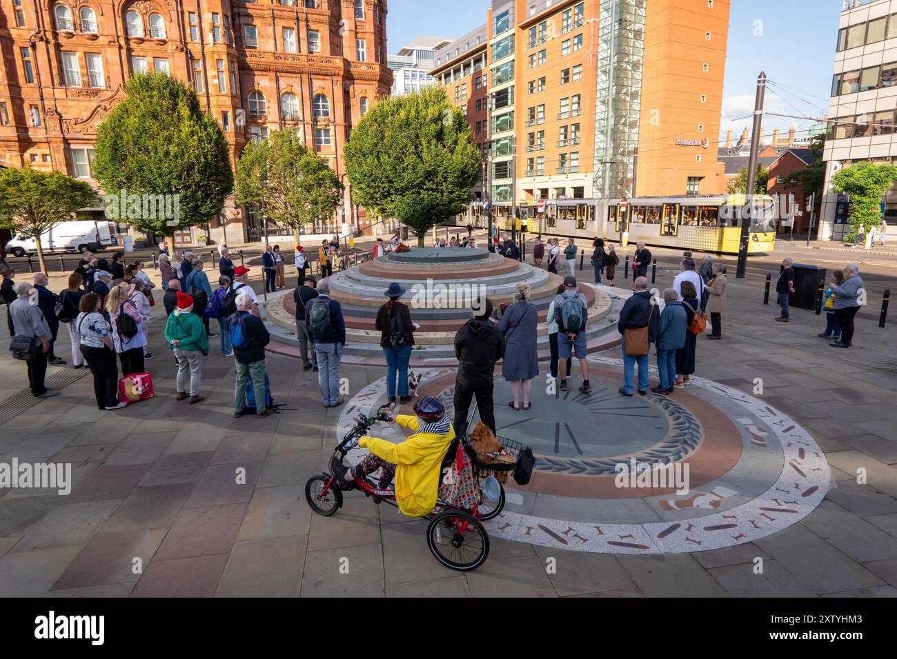 Manchester, Regno Unito 16 agosto 2024 una piccola folla si riunisce nel luogo del massacro di Peterloo del 1819 con corone e fiori rimasti. L'evento è stato quello di commemorare l'evento in cui soldati e miliziani hanno ucciso 18 persone e ferito centinaia delle 60.000 persone, che protestavano contro le cattive condizioni di lavoro che invocavano la democrazia parlamentare. Il loro incontro fu determinante nello sviluppo dei sindacati e nell'ottenimento dei diritti di voto. In precedenza le proteste dei gruppi di persone disabili si sono lamentate che il monumento non è accessibile. Peterloo Memorial, Manchester, Regno Unito. Credito: GaryRobertsphotograph Foto Stock