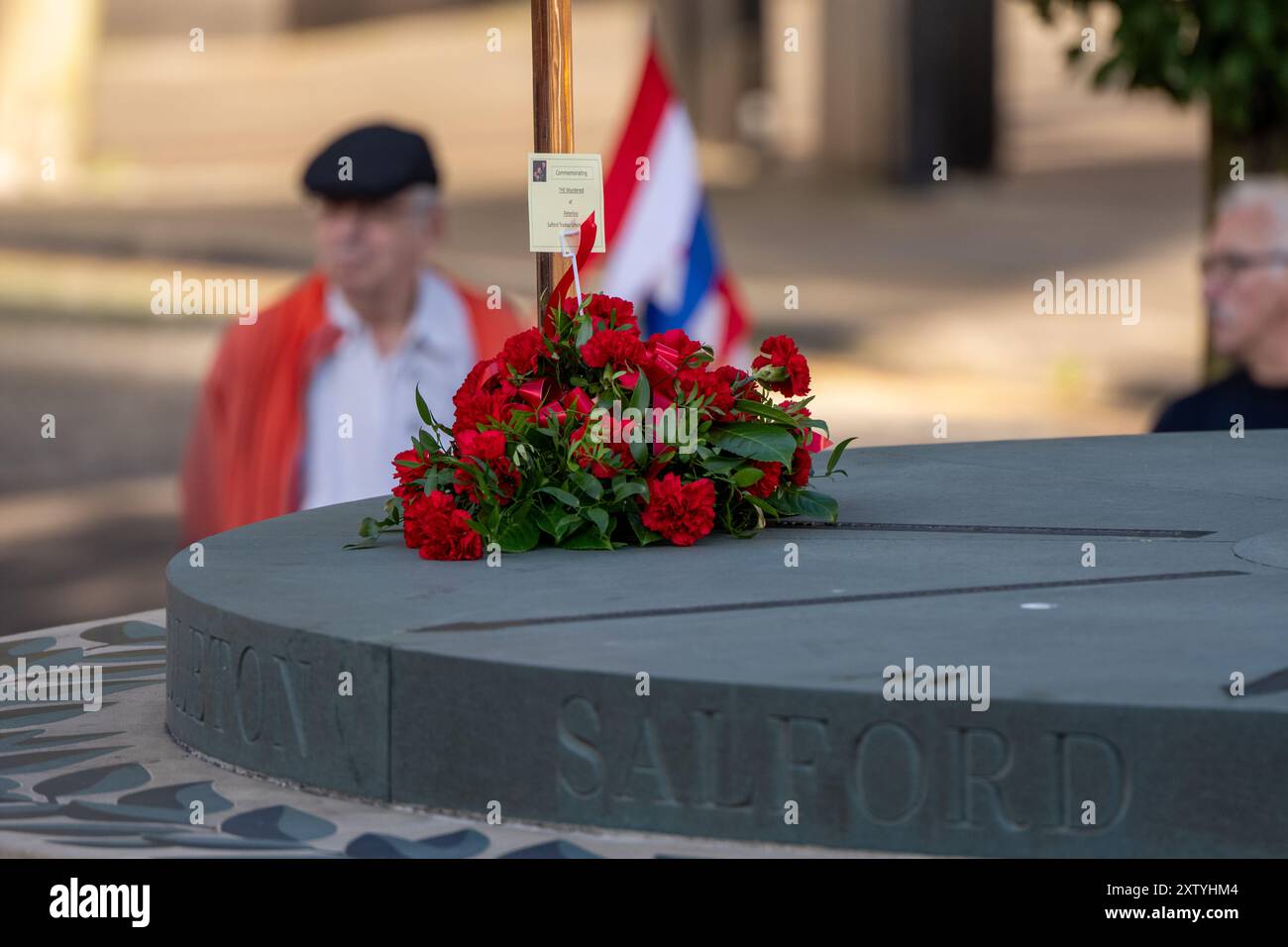 Manchester, Regno Unito 16 agosto 2024 una piccola folla si riunisce nel luogo del massacro di Peterloo del 1819 con corone e fiori rimasti. L'evento è stato quello di commemorare l'evento in cui soldati e miliziani hanno ucciso 18 persone e ferito centinaia delle 60.000 persone, che protestavano contro le cattive condizioni di lavoro che invocavano la democrazia parlamentare. Il loro incontro fu determinante nello sviluppo dei sindacati e nell'ottenimento dei diritti di voto. In precedenza le proteste dei gruppi di persone disabili si sono lamentate che il monumento non è accessibile. Peterloo Memorial, Manchester, Regno Unito. Credito: GaryRobertsphotograph Foto Stock