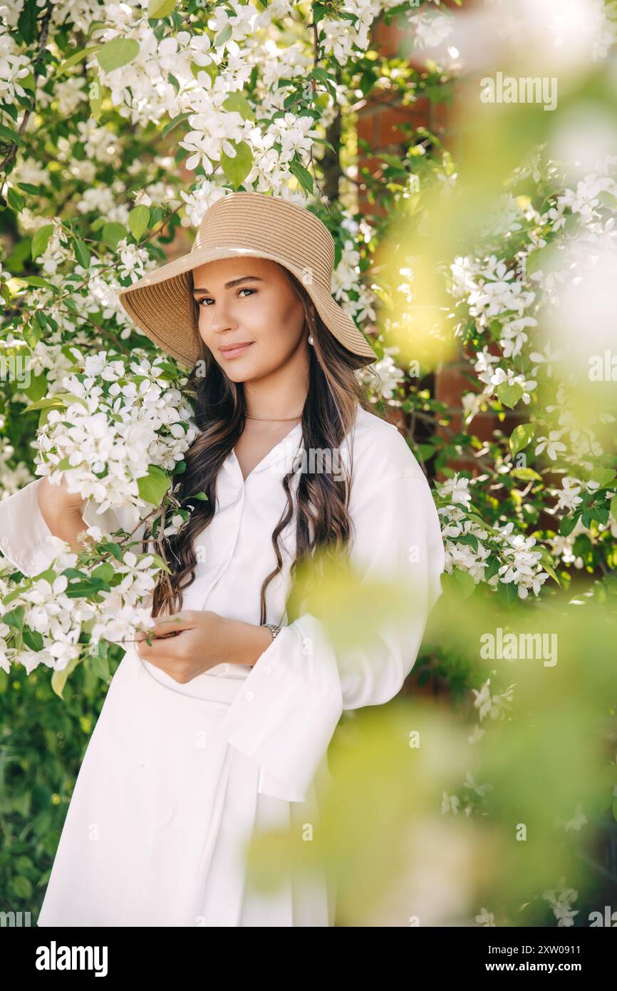 Una bella giovane donna con un cappello e abiti bianchi in un giardino fiorito Foto Stock