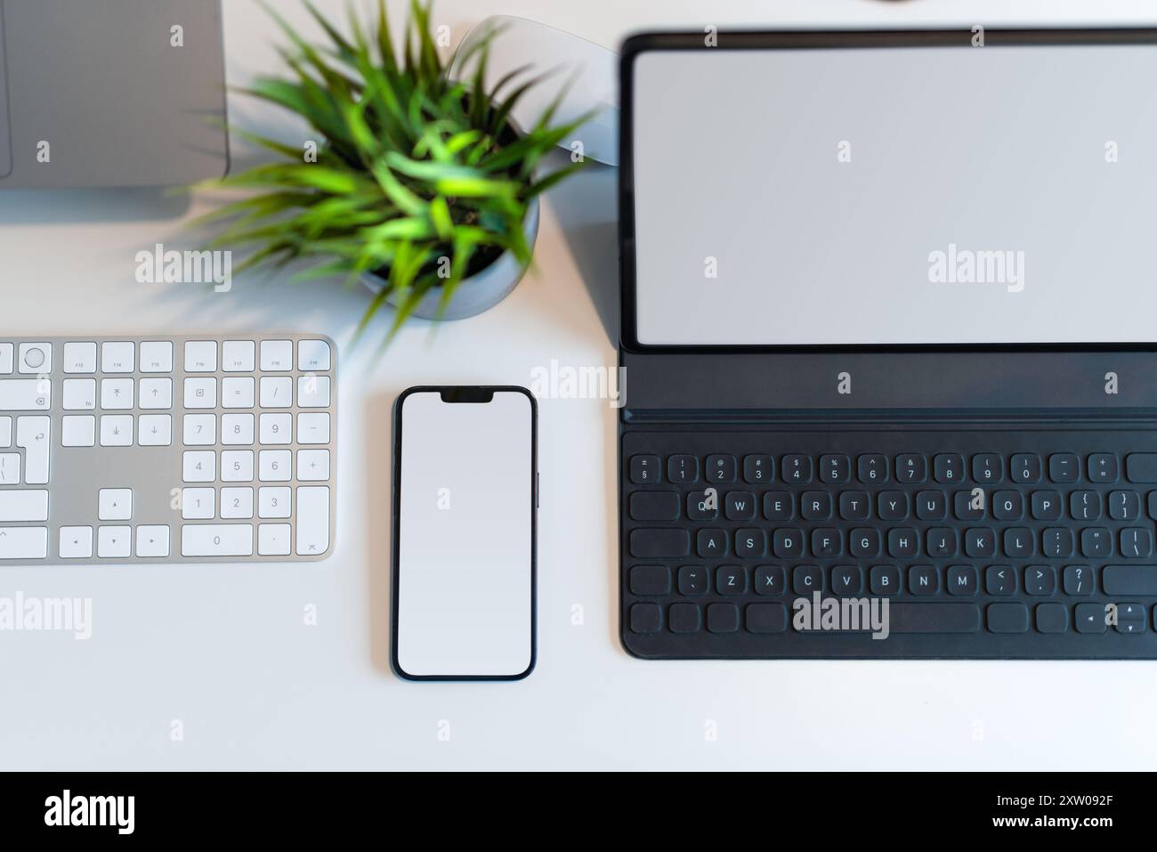 Smartphone, laptop, tablet grafico, modelli a schermo vuoto. Tabella con vista dall'alto con impianto e tastiera. Foto Stock