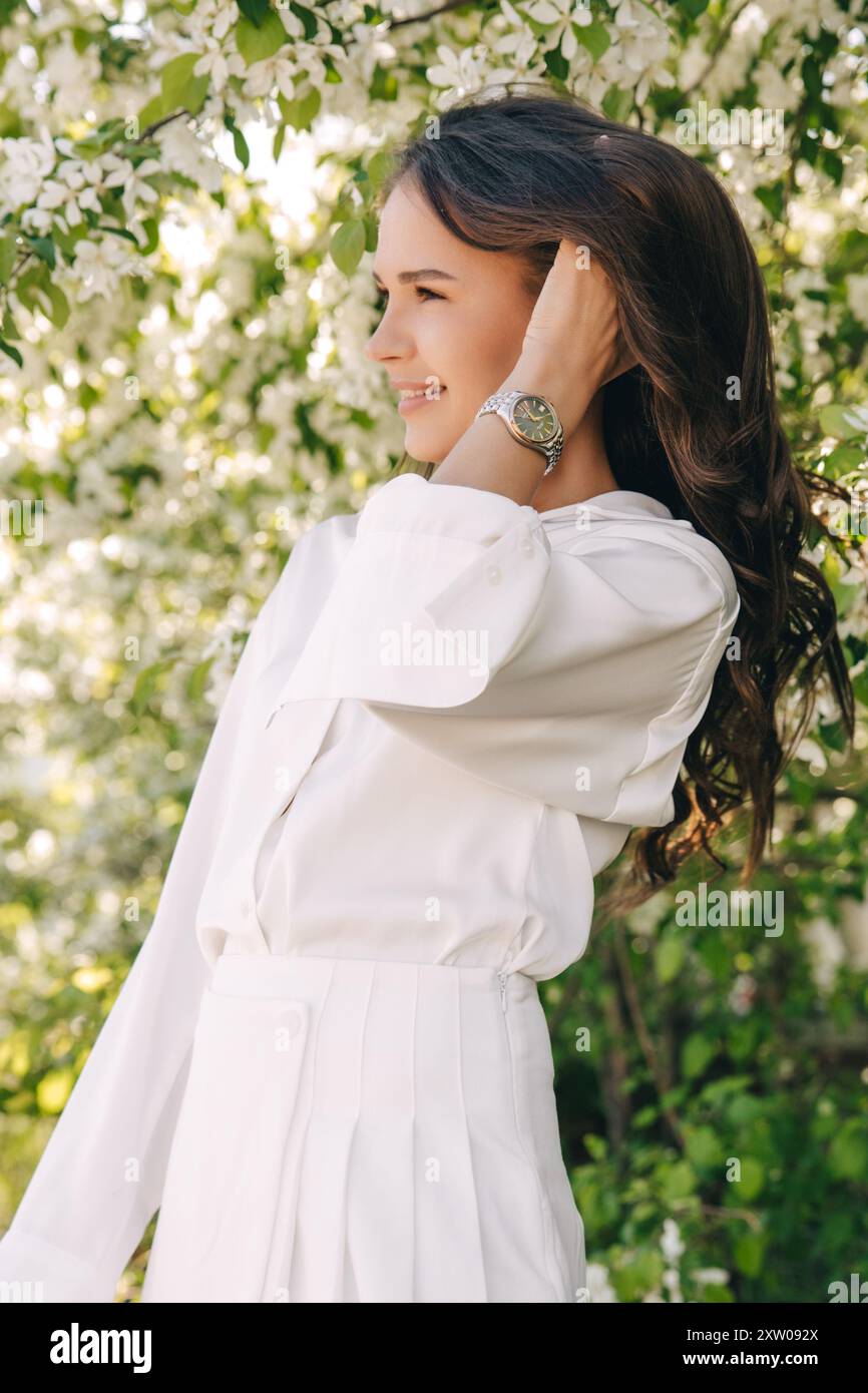 Ritratto di una bella ragazza con i capelli lunghi vicino a un albero in fiore in abiti bianchi alla moda Foto Stock