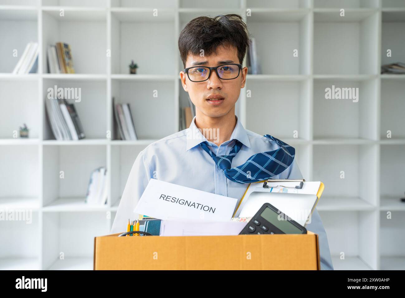 Triste giovane uomo d'affari che tiene una cassa piena di cose del suo ufficio mentre esce dal suo ufficio dopo aver lasciato il lavoro Foto Stock