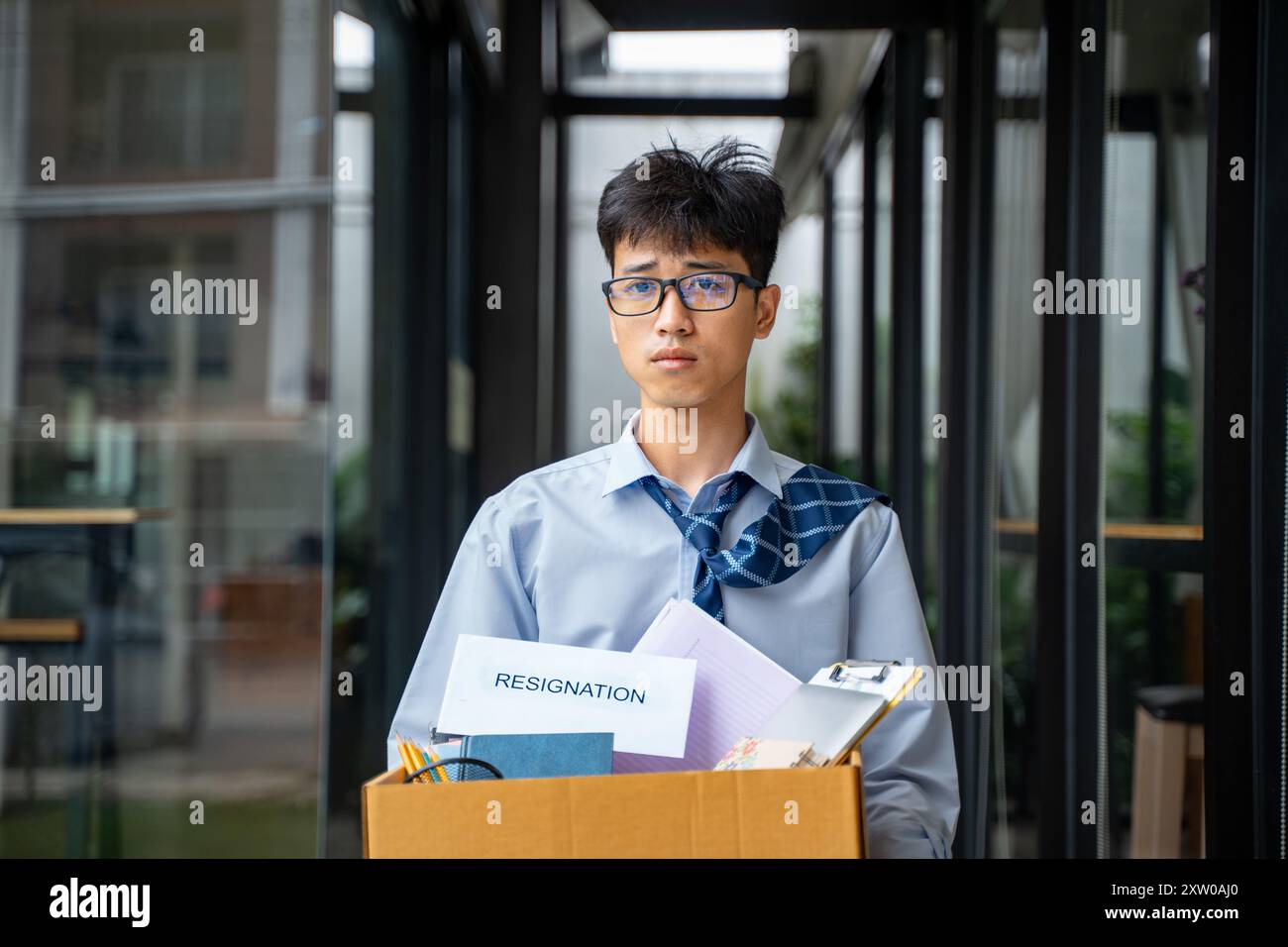 Triste giovane uomo d'affari che tiene una cassa piena di cose del suo ufficio mentre esce dal suo ufficio dopo aver lasciato il lavoro Foto Stock