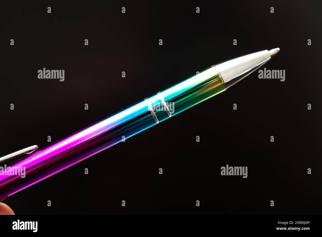 Una penna arcobaleno colorata con una finitura lucida appoggiata su uno sfondo scuro, perfetta per illustrare creatività, scrittura ed espressione artistica. IDE Foto Stock