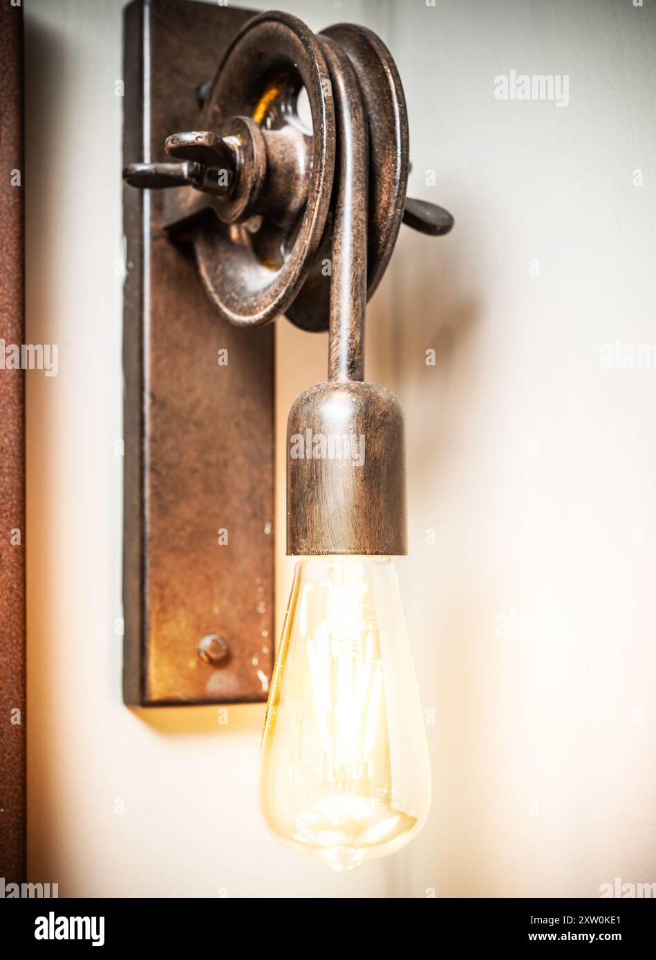 Un applique rustico presenta una lampadina Edison e un design a puleggia vintage, che aggiungono un fascino unico agli interni in stile industriale o agli spazi contemporanei. Foto Stock