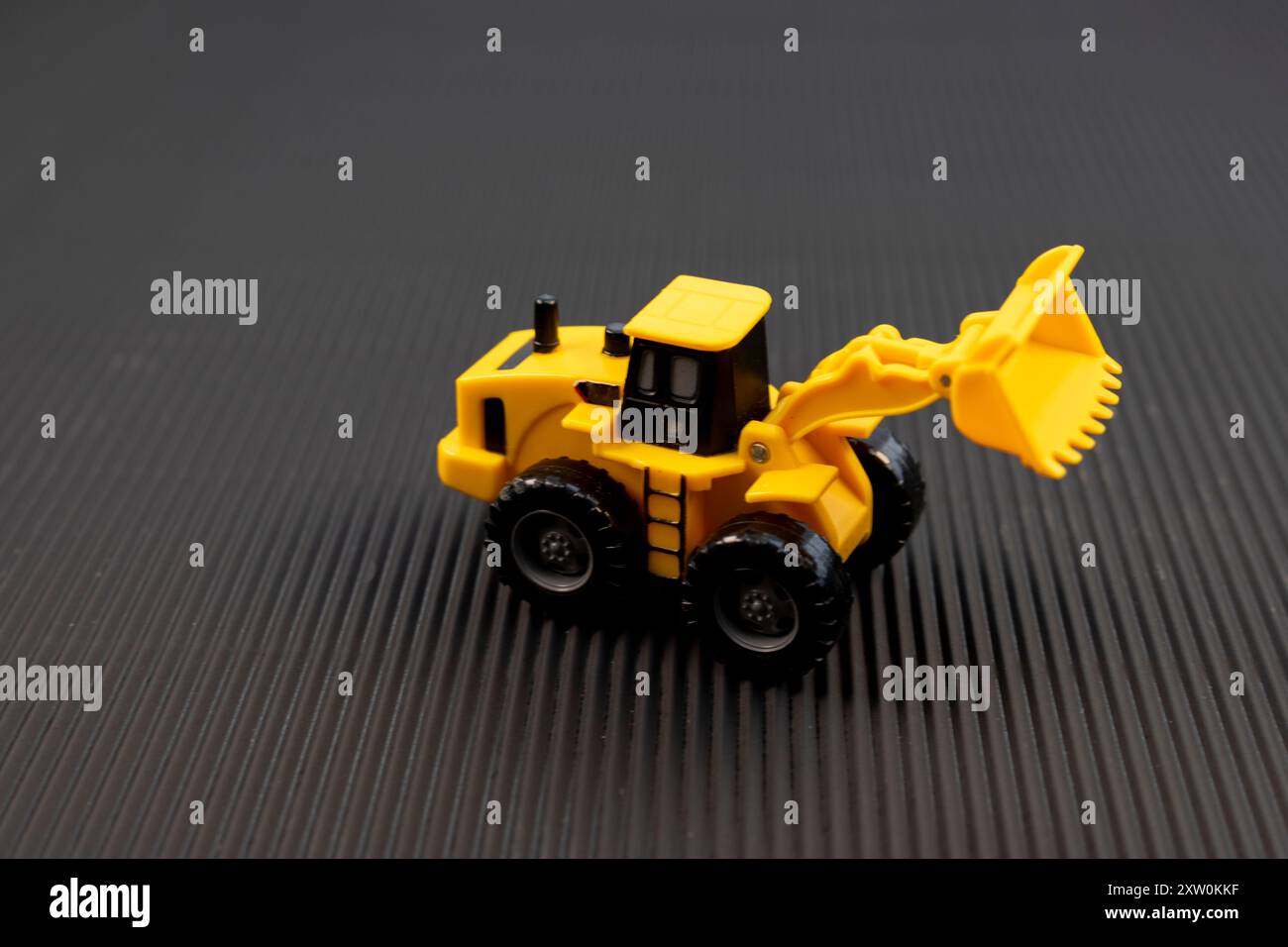 Caricatore giocattolo giallo su sfondo nero testurizzato. Concetto di macchinari pesanti. Foto Stock