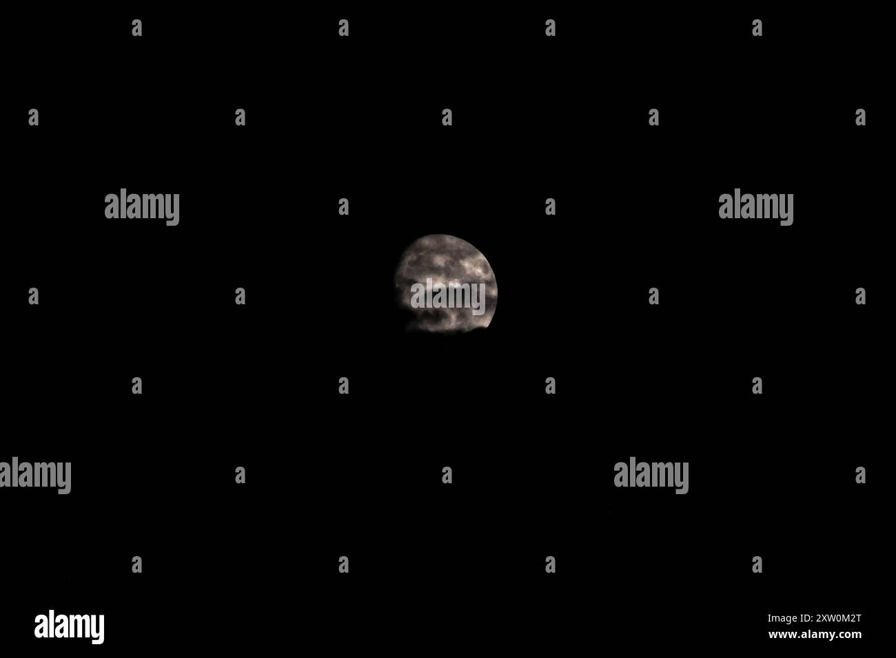 La luna è parzialmente oscurata dalle nuvole nel cielo notturno buio Foto Stock