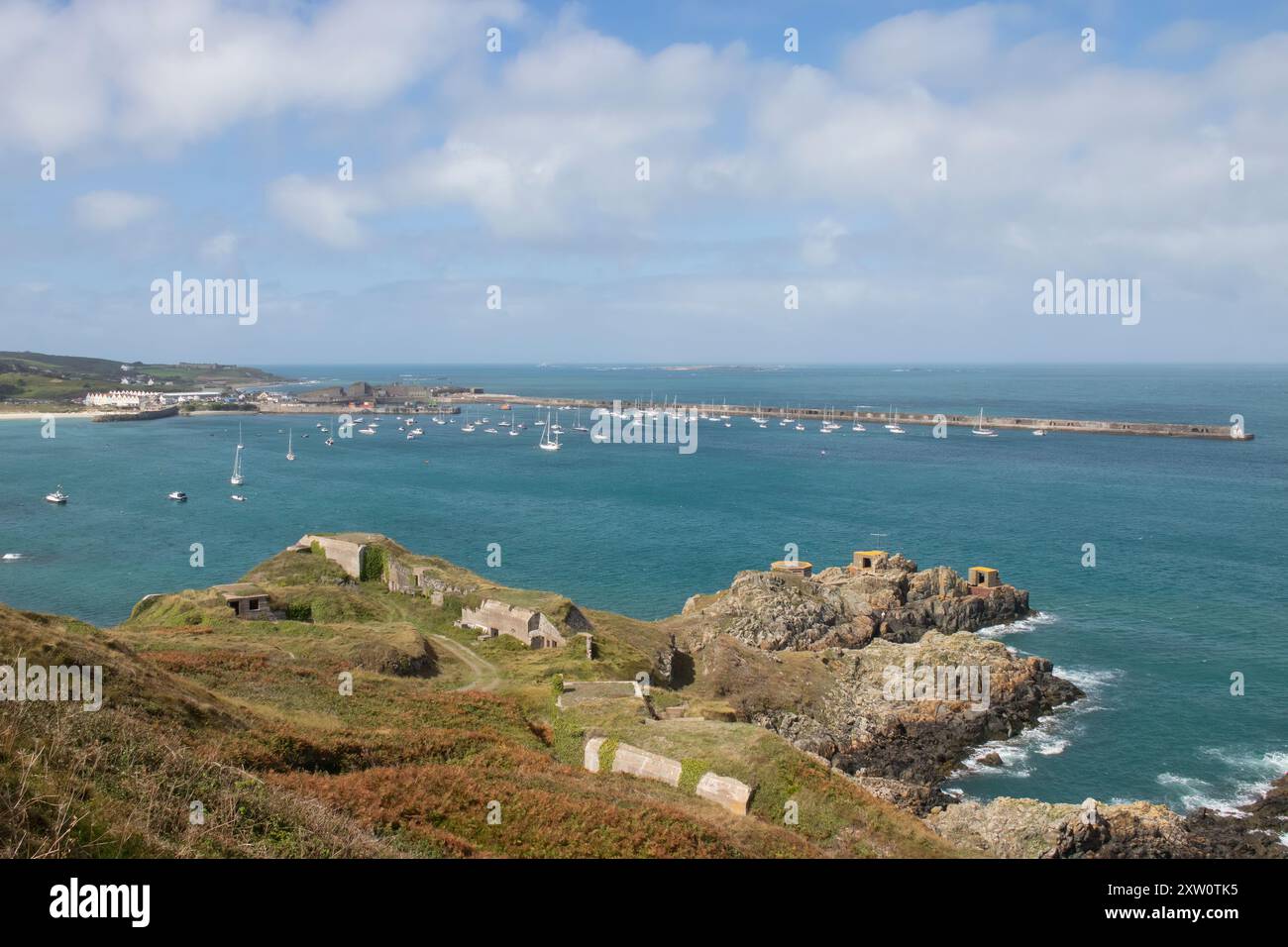 Ammira la scena del porto e della spiaggia delle isole del Canale di Alderney con le fortificazioni tedesche della seconda guerra mondiale sulle colline Foto Stock