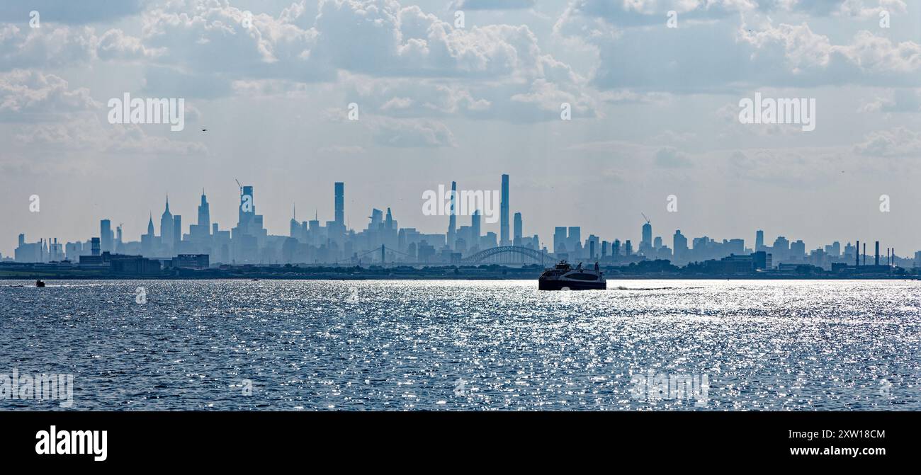 Nuvoloso, nebbioso, skyline di New York nel tardo pomeriggio, visto da Ferry Point/Throggs Neck, Bronx, con Rikers Island (prigione) in primo piano. Foto Stock