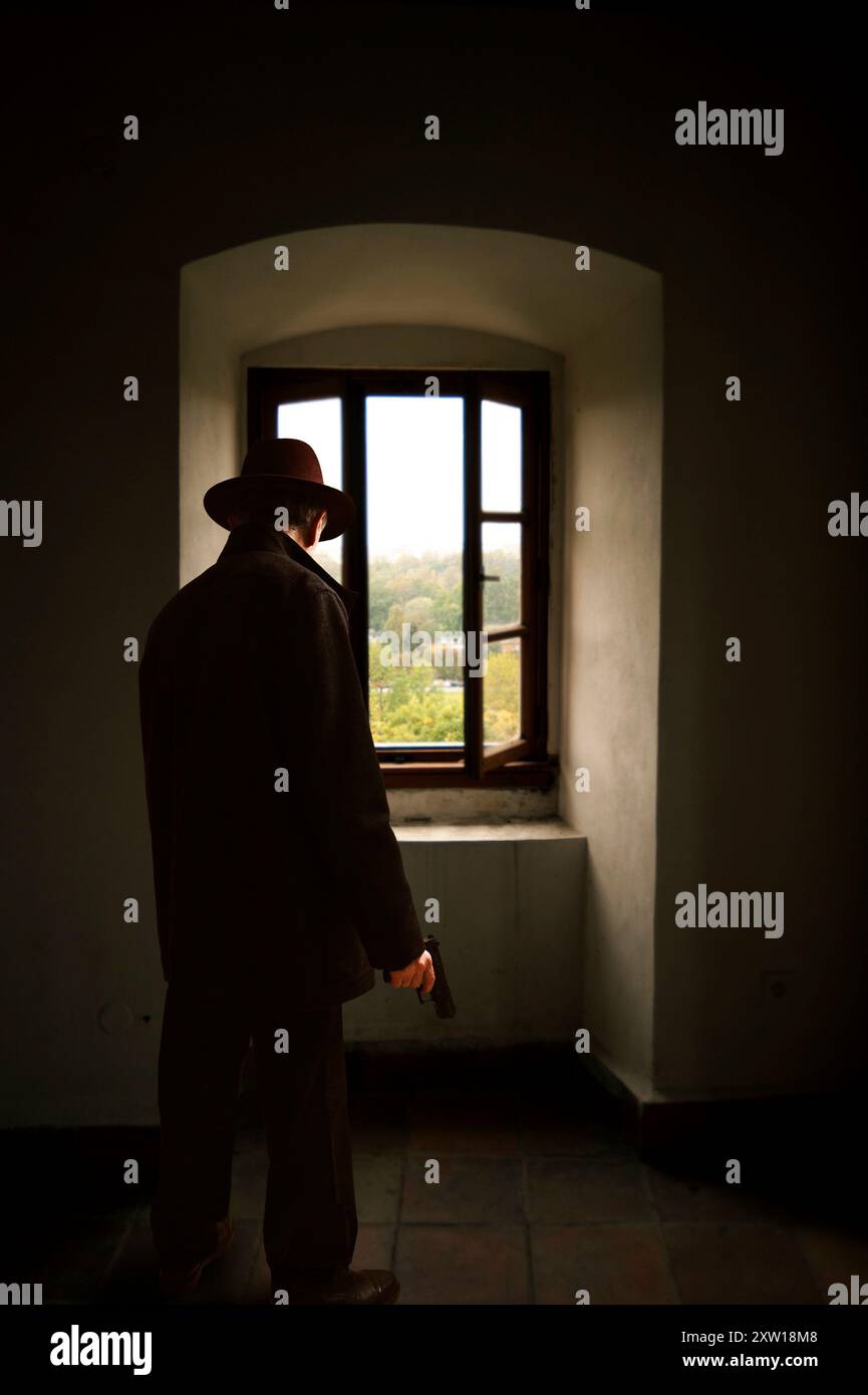 uomo che indossa un cappello fedora e tiene una pistola all'interno di un edificio Foto Stock