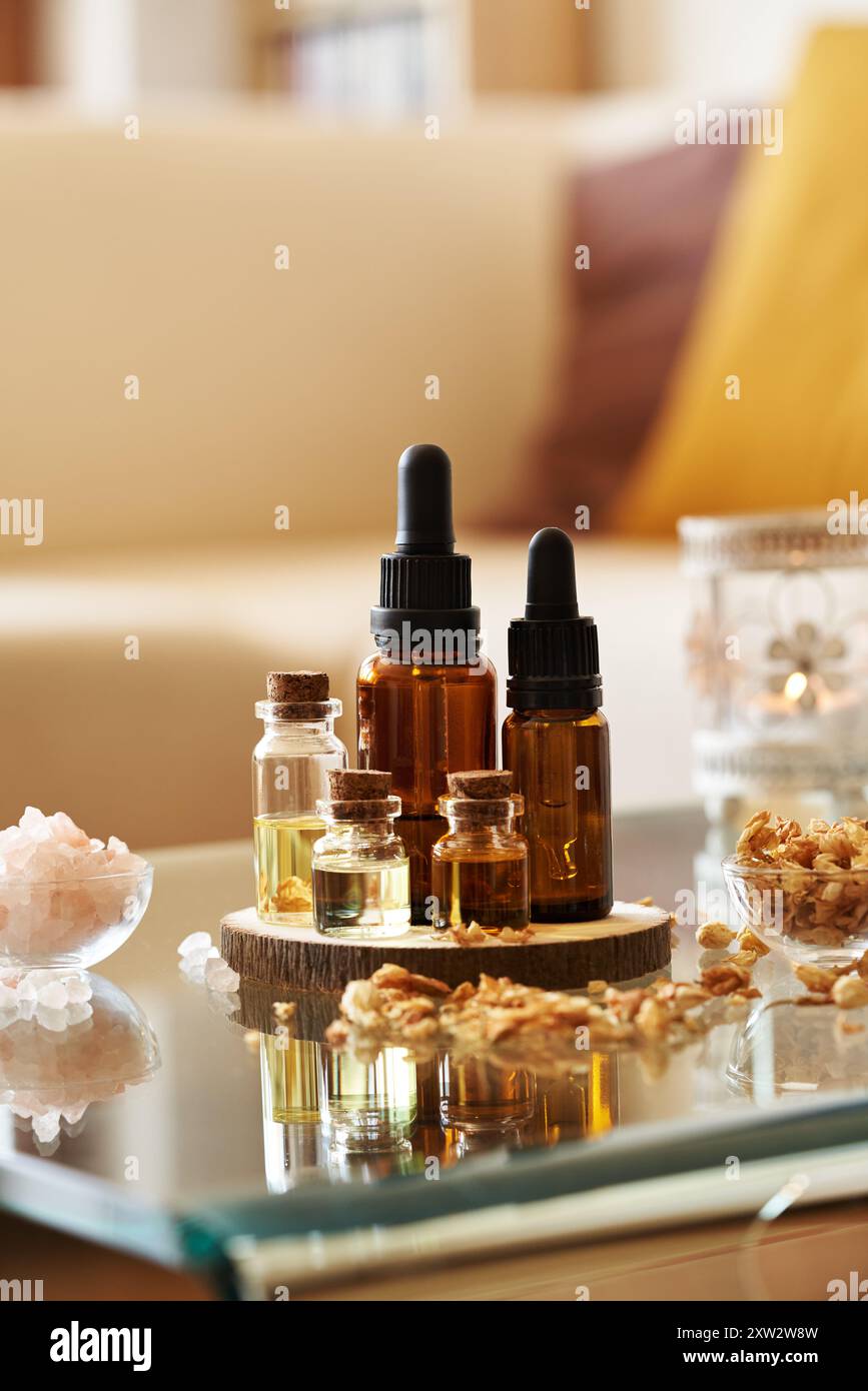Diverse bottiglie di olio essenziale per aromaterapia con sale marino rosa dell'Himalaya, erbe secche e candele a casa Foto Stock