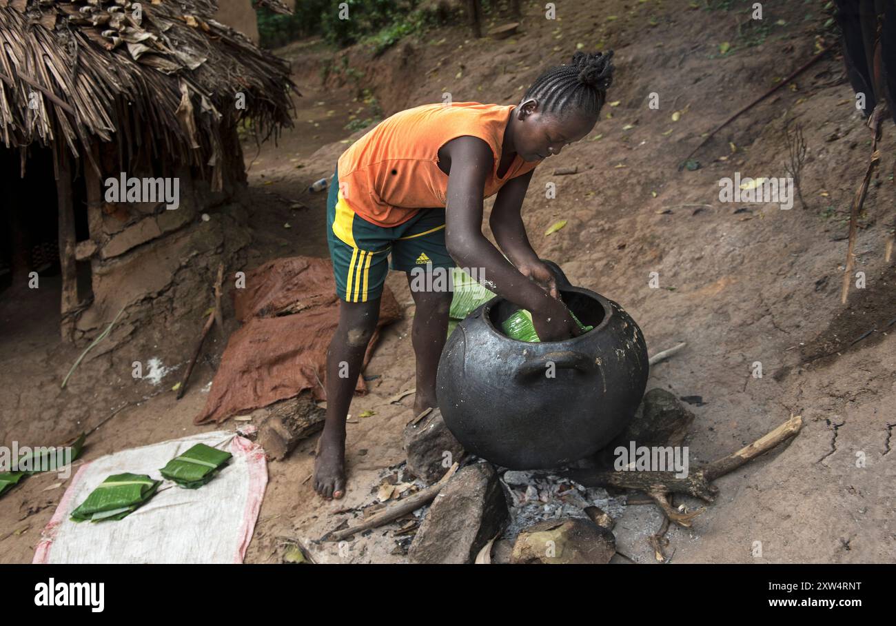 Una giovane donna del gruppo etnico Ari colloca foglie di banana ripiene in una pentola di argilla sopra il fuoco aperto per cucinare, nella valle meridionale dell'Omo, in Etiopia Foto Stock