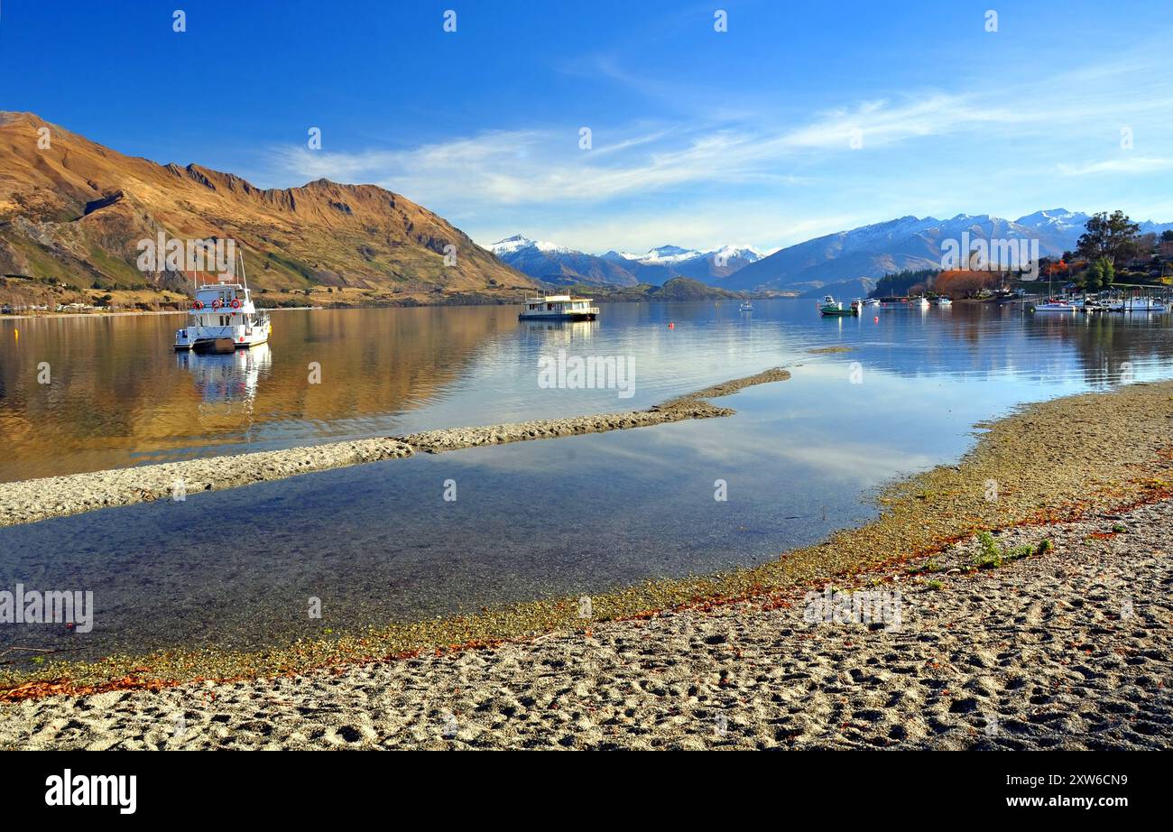 Il lago Wanaka e barche con il Sud delle Alpi in background. Central Otago, Nuova Zelanda. In primo piano nota come basso il livello del lago è dopo uno Foto Stock