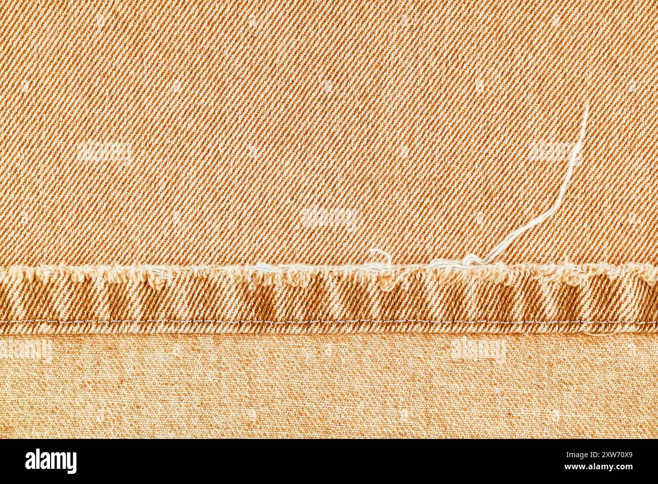 Pantaloni in jeans in denim arancione con bordo scabro su fondo in tessuto jean, primo piano, macro. Jeans strappati, distrutti strappati. Carta da parati, sfondo, design detai Foto Stock